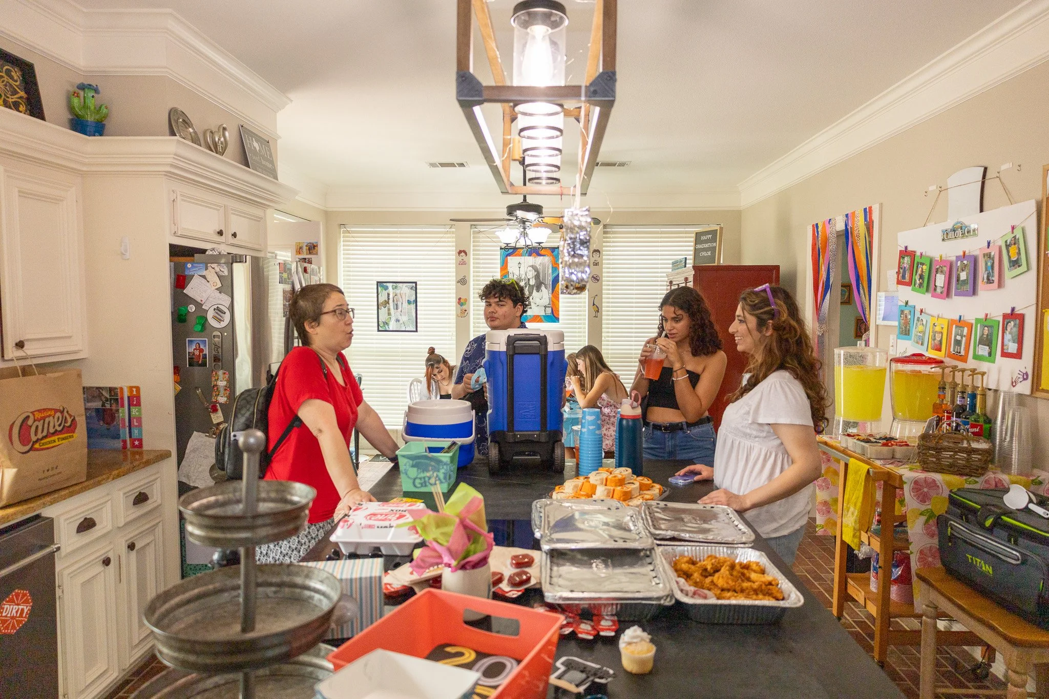 People gathered in a kitchen at a party, with food and drinks on the table.