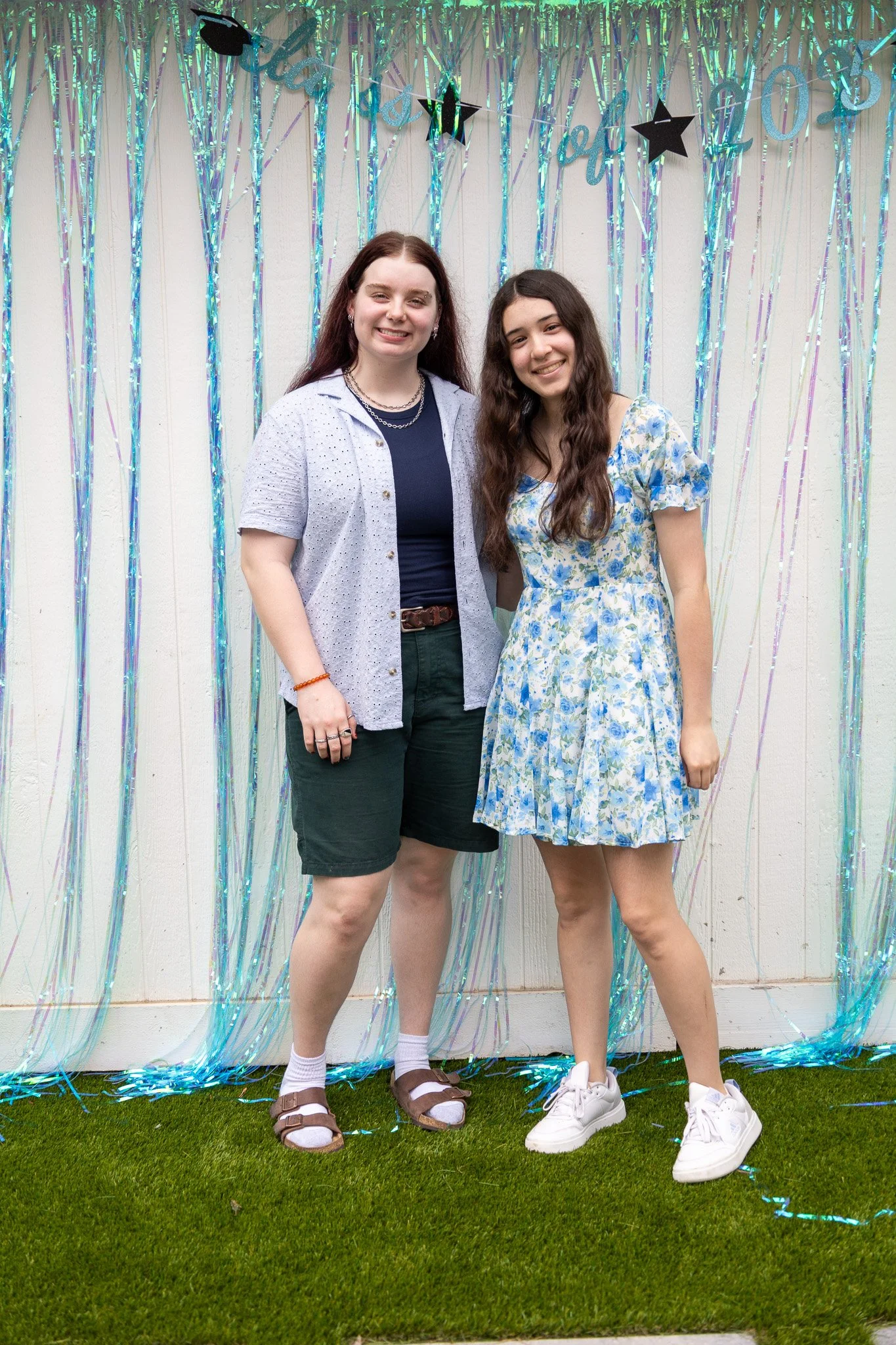 Two young women standing in front of a decorated backdrop with shiny streamers and stars, smiling at the camera.
