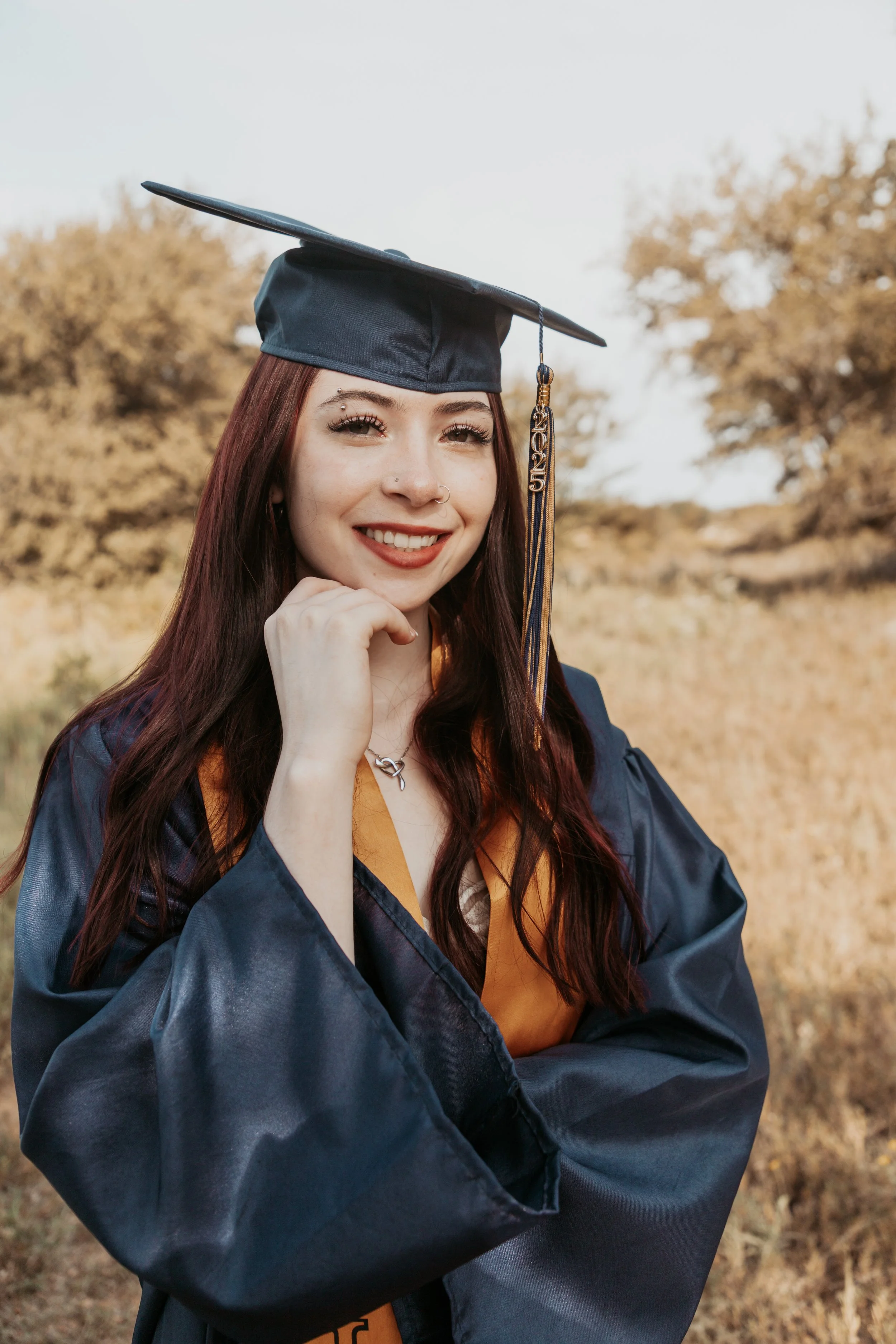 A young woman in a graduation cap and gown smiling outdoors.