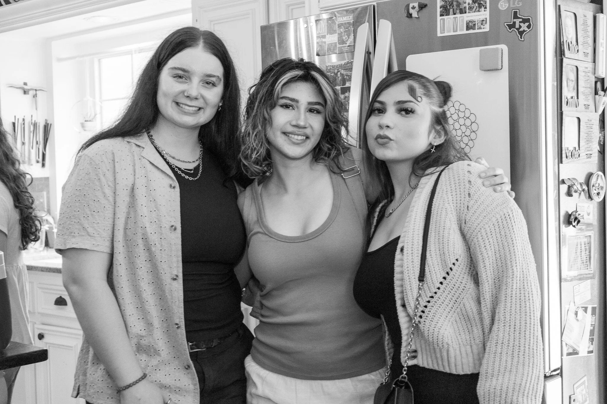 Three women standing close together in a kitchen, smiling and posing for a photo.