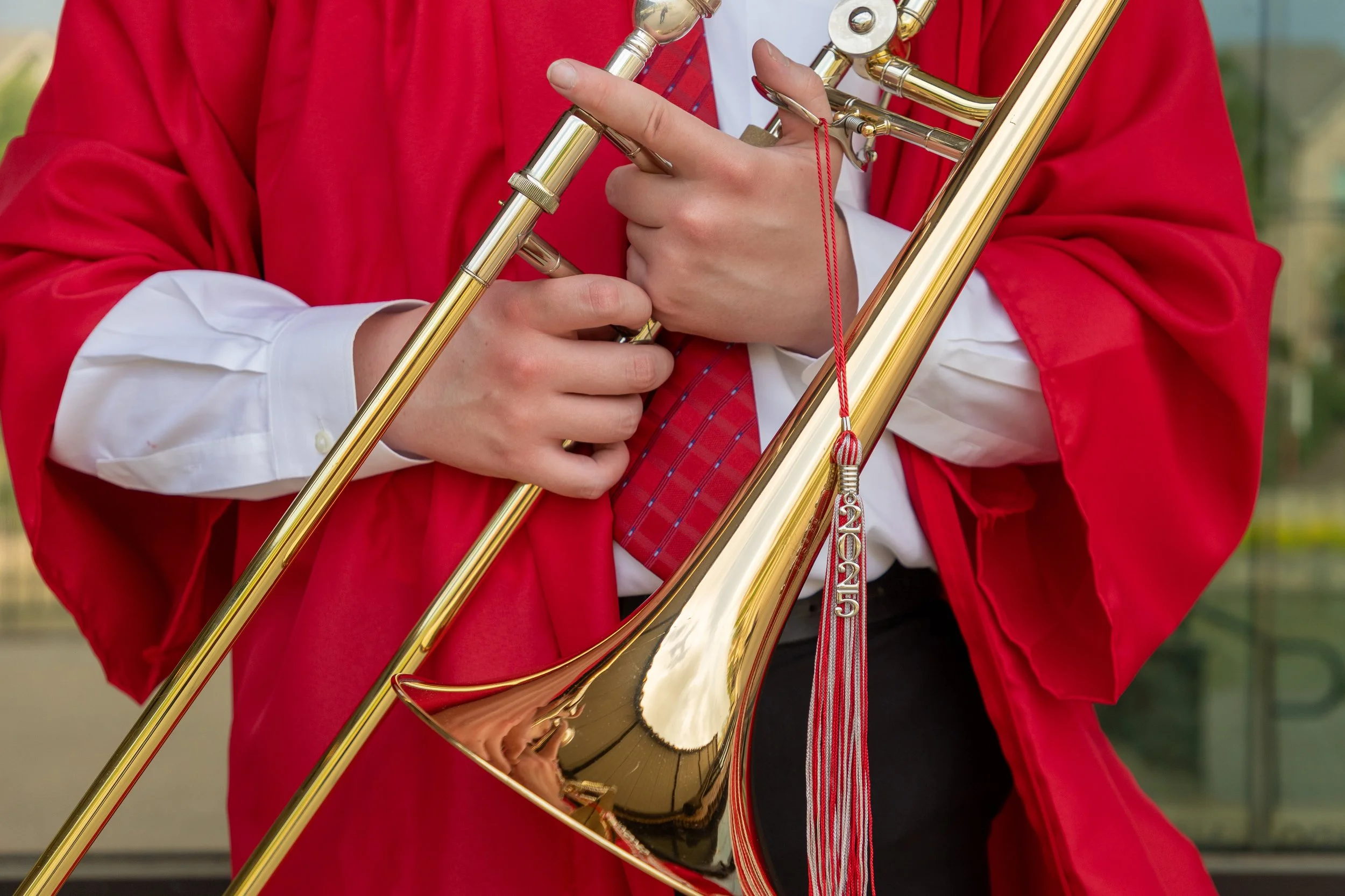 Person in a red jacket holding a golden trombone, wearing a white shirt and red plaid tie.