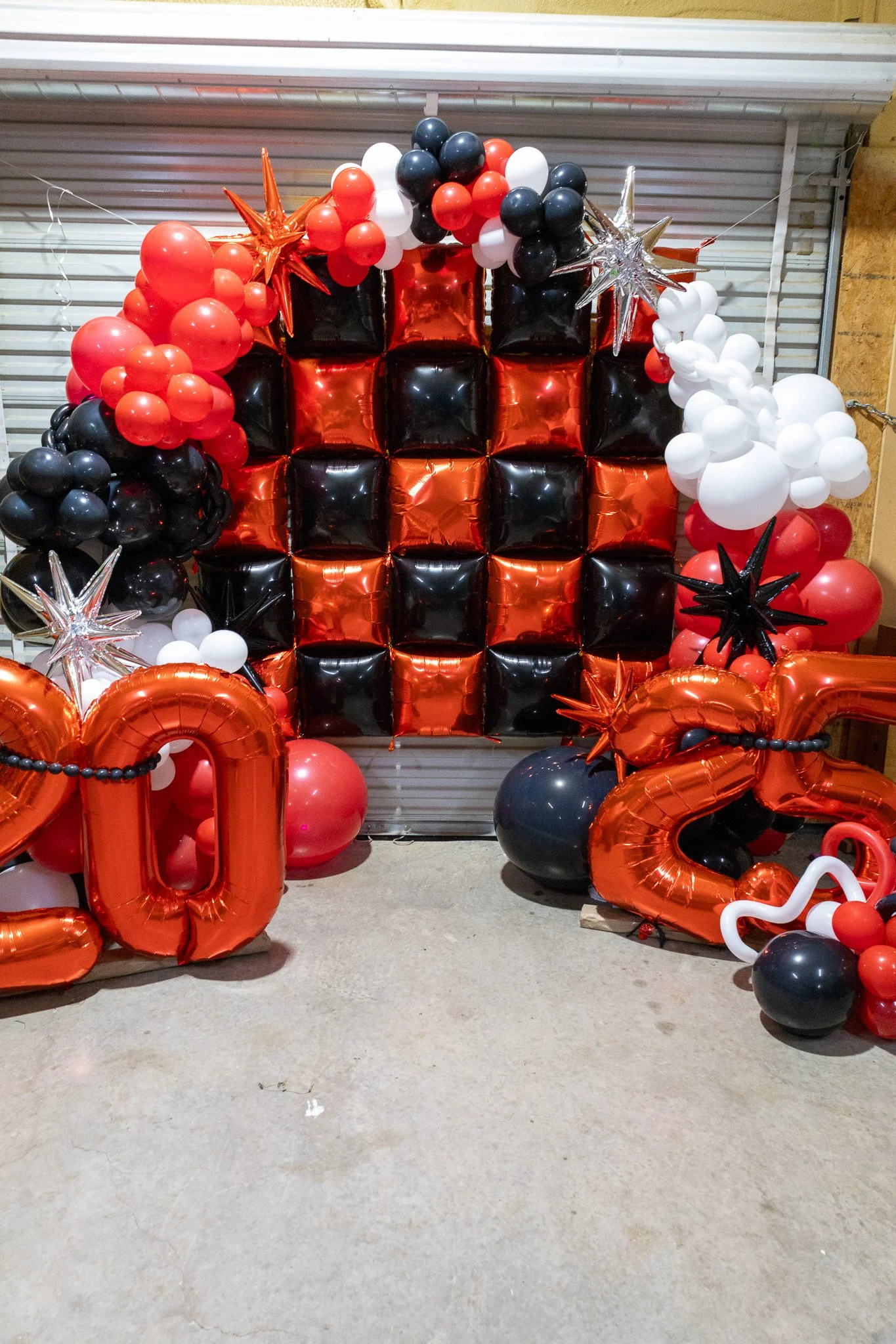 Decorative balloon backdrop with black, red, and white balloons, including star-shaped balloons, and large metallic number balloons '0' and '2' for celebration.