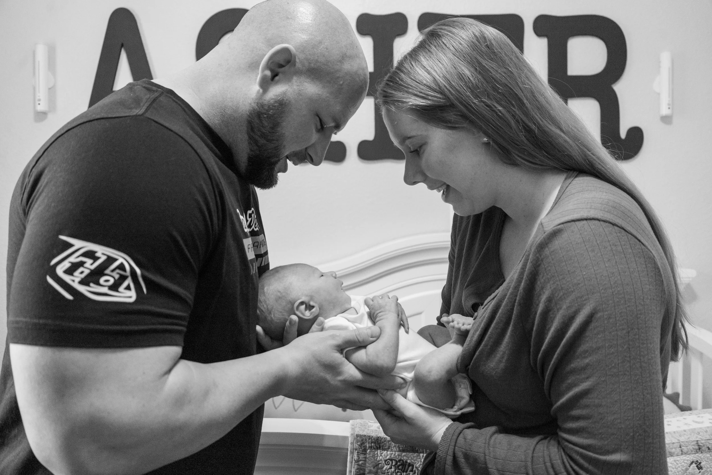 A man and woman are smiling at a newborn baby, who they are holding and looking at lovingly.