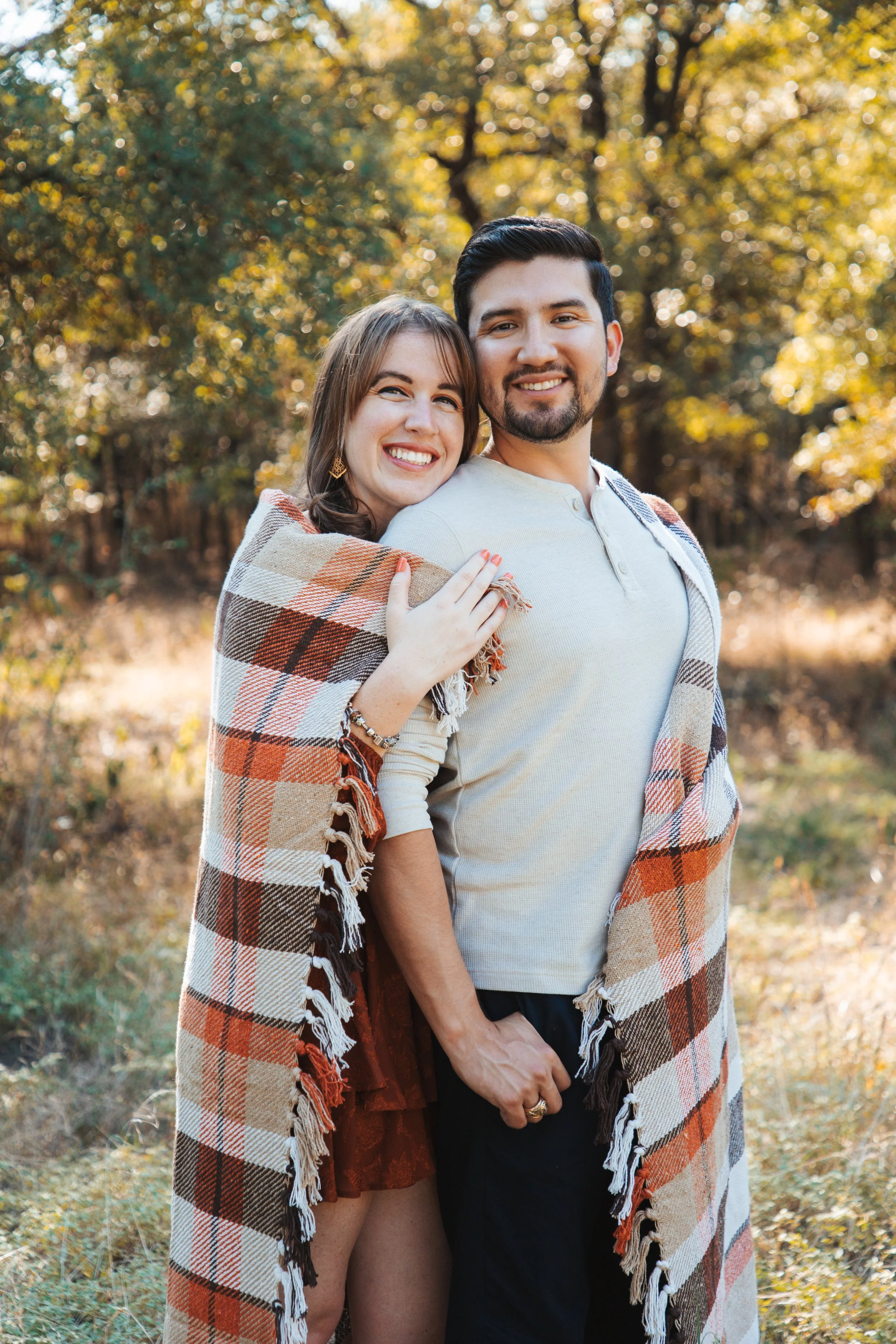 Happy couple wrapped in a plaid blanket outdoors in a forest during fall.