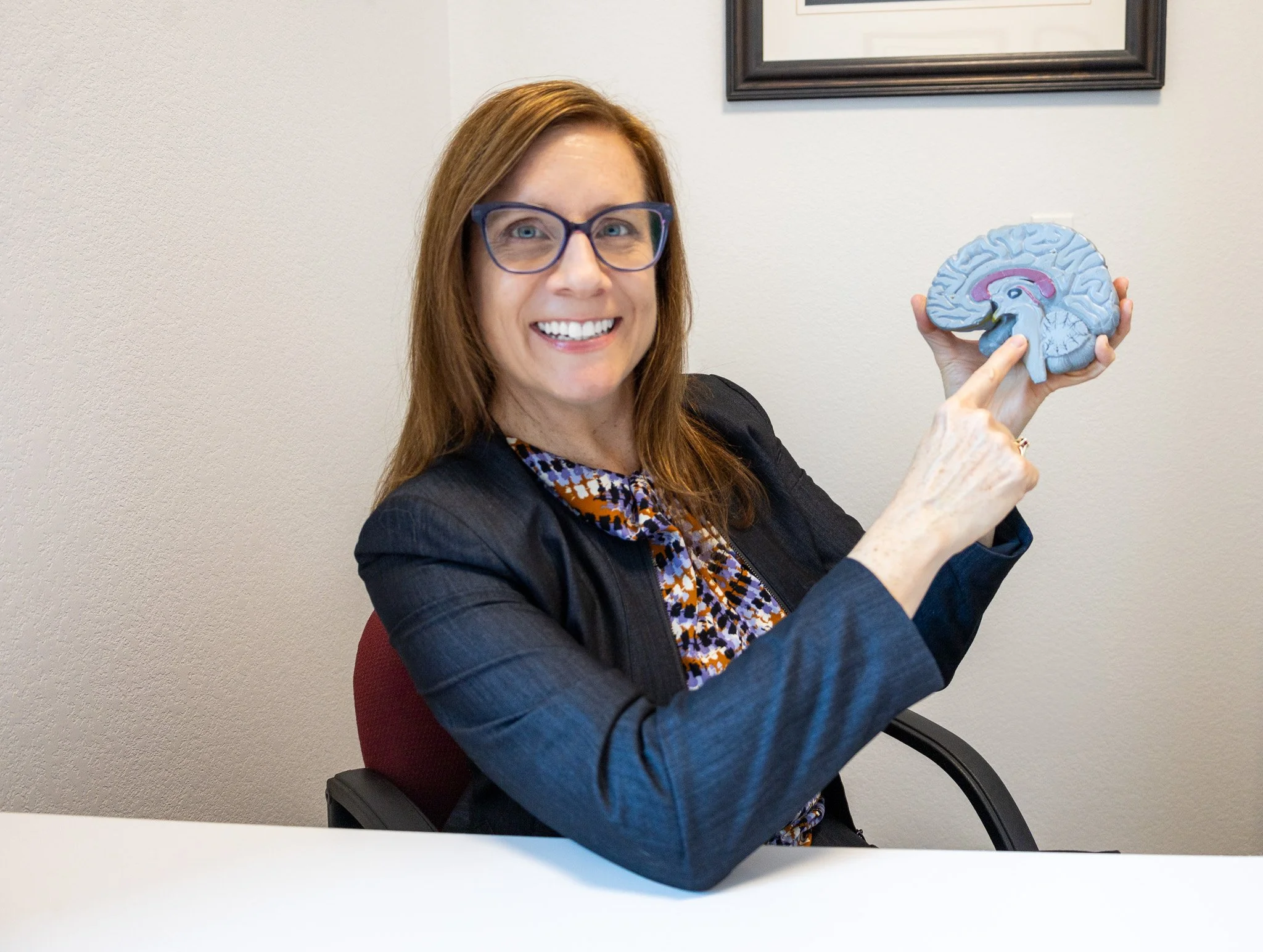 Woman with red hair and glasses holding a model of a brain.