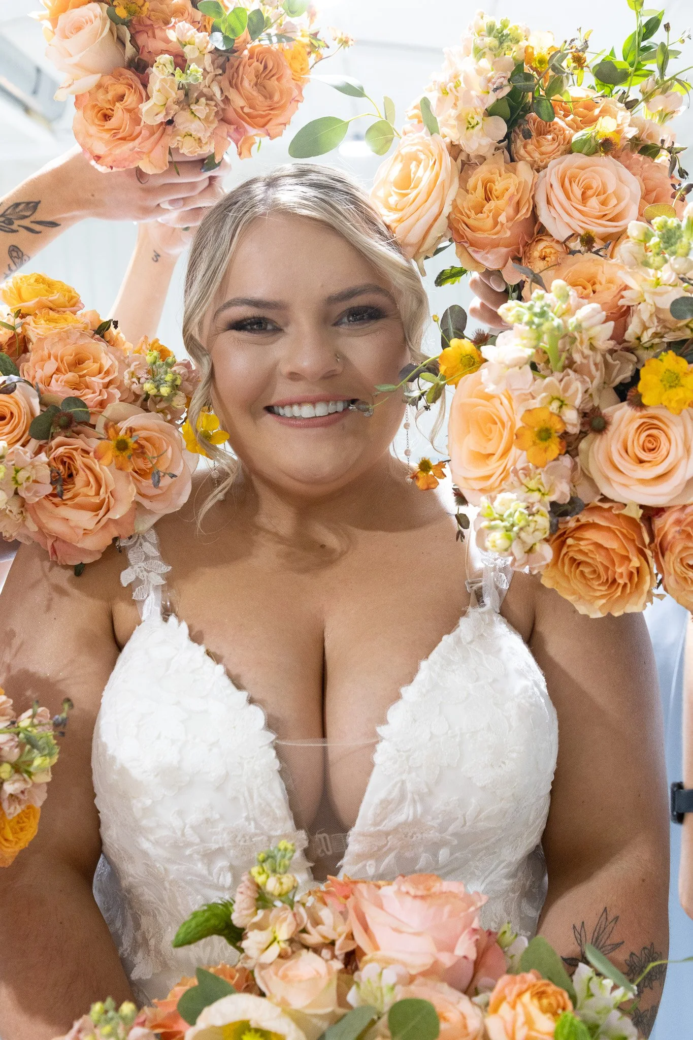 A smiling bride in a white wedding dress surrounded by peach and yellow flowers.