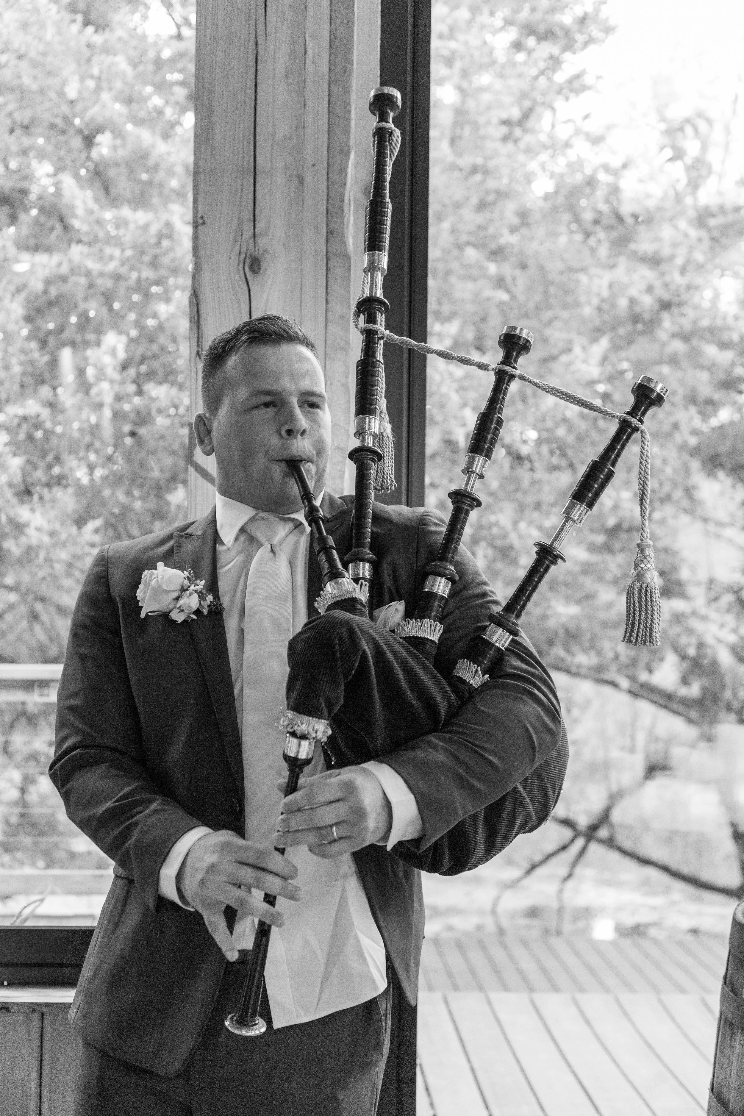 Man in a suit playing bagpipes during a wedding ceremony.