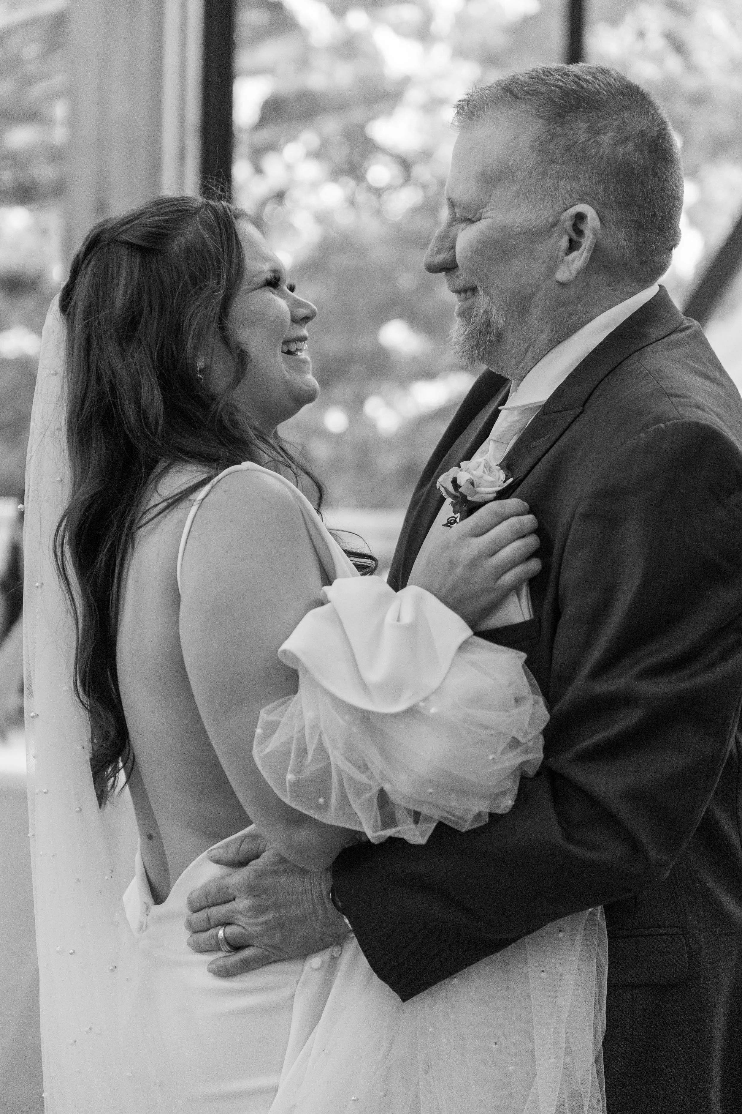 A bride and an older man, likely her father, sharing a joyful dance at her wedding, both smiling and looking at each other.