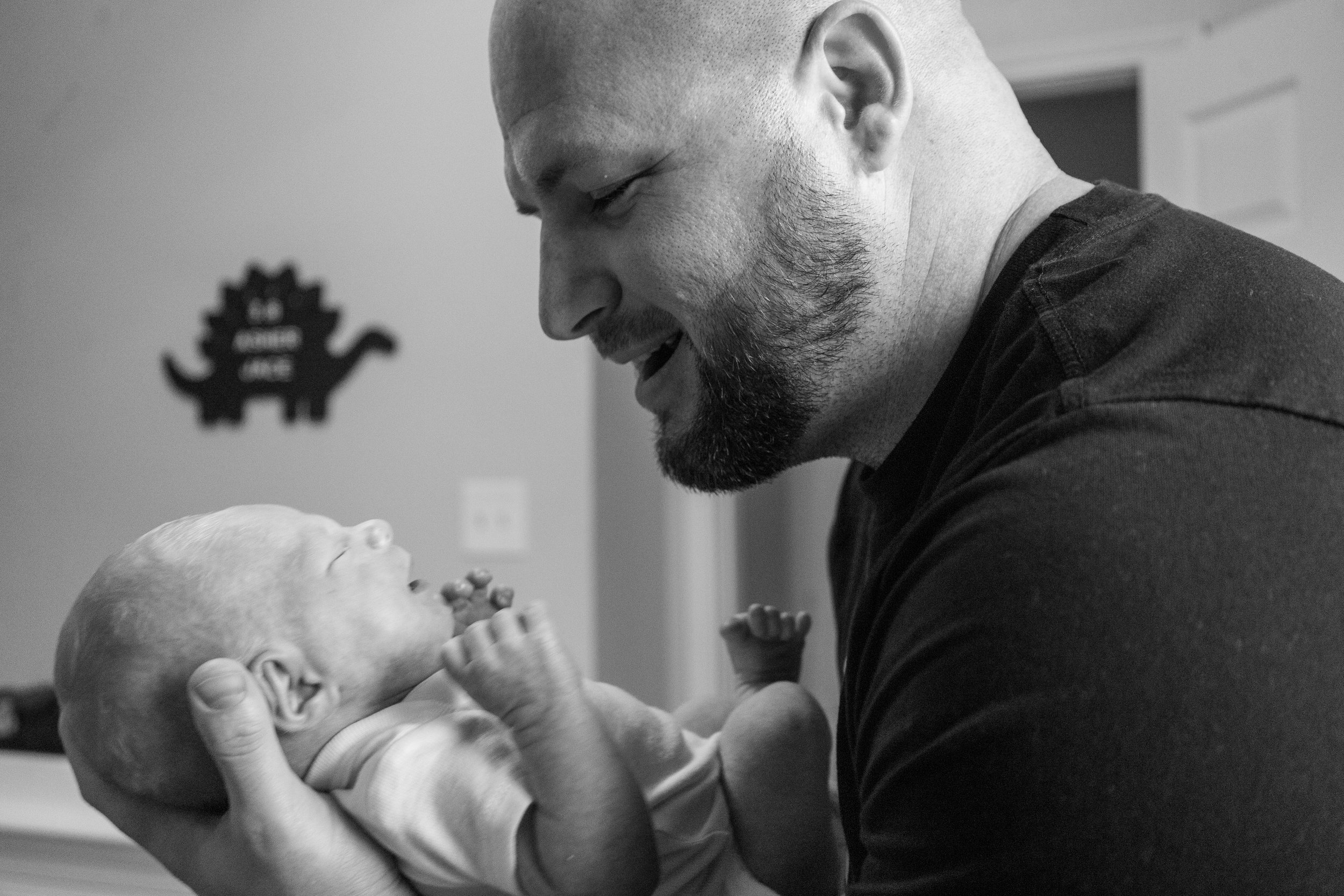 A man holding a newborn baby in a home setting, looking lovingly at the baby in black-and-white.