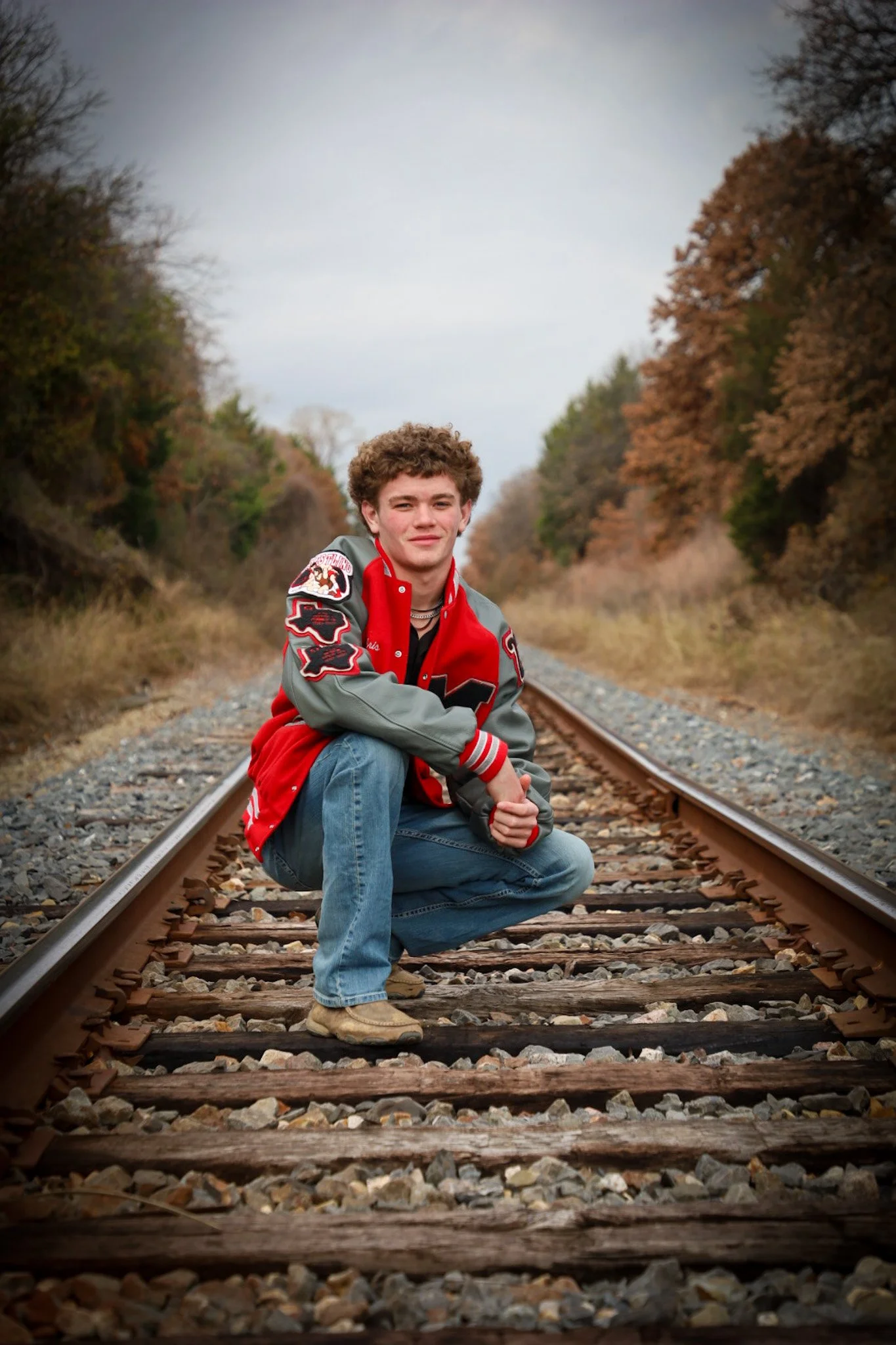 A young man crouching on a railroad track surrounded by autumn trees.