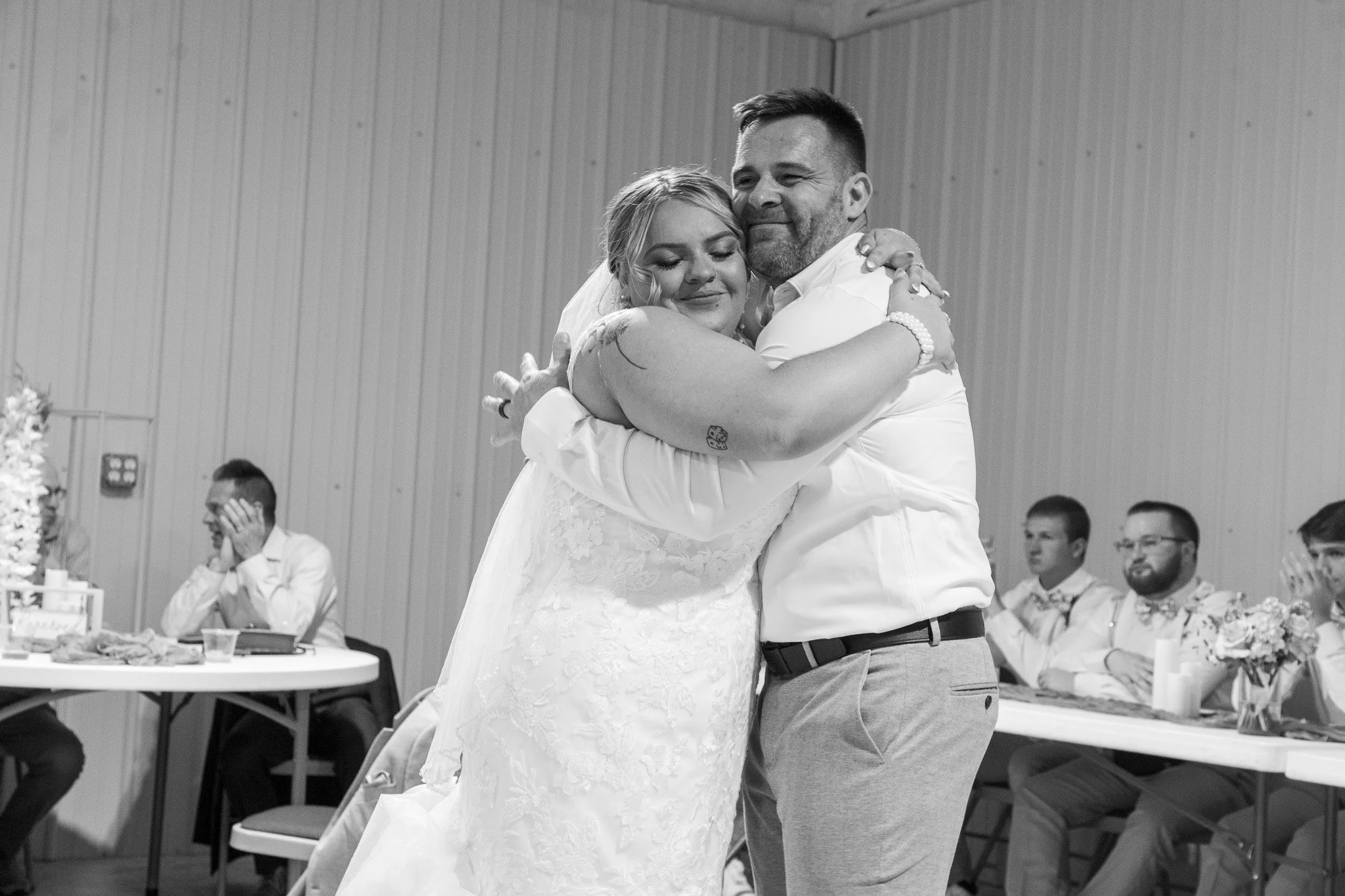 A bride and groom are hugging during their wedding reception, with guests watching in the background.