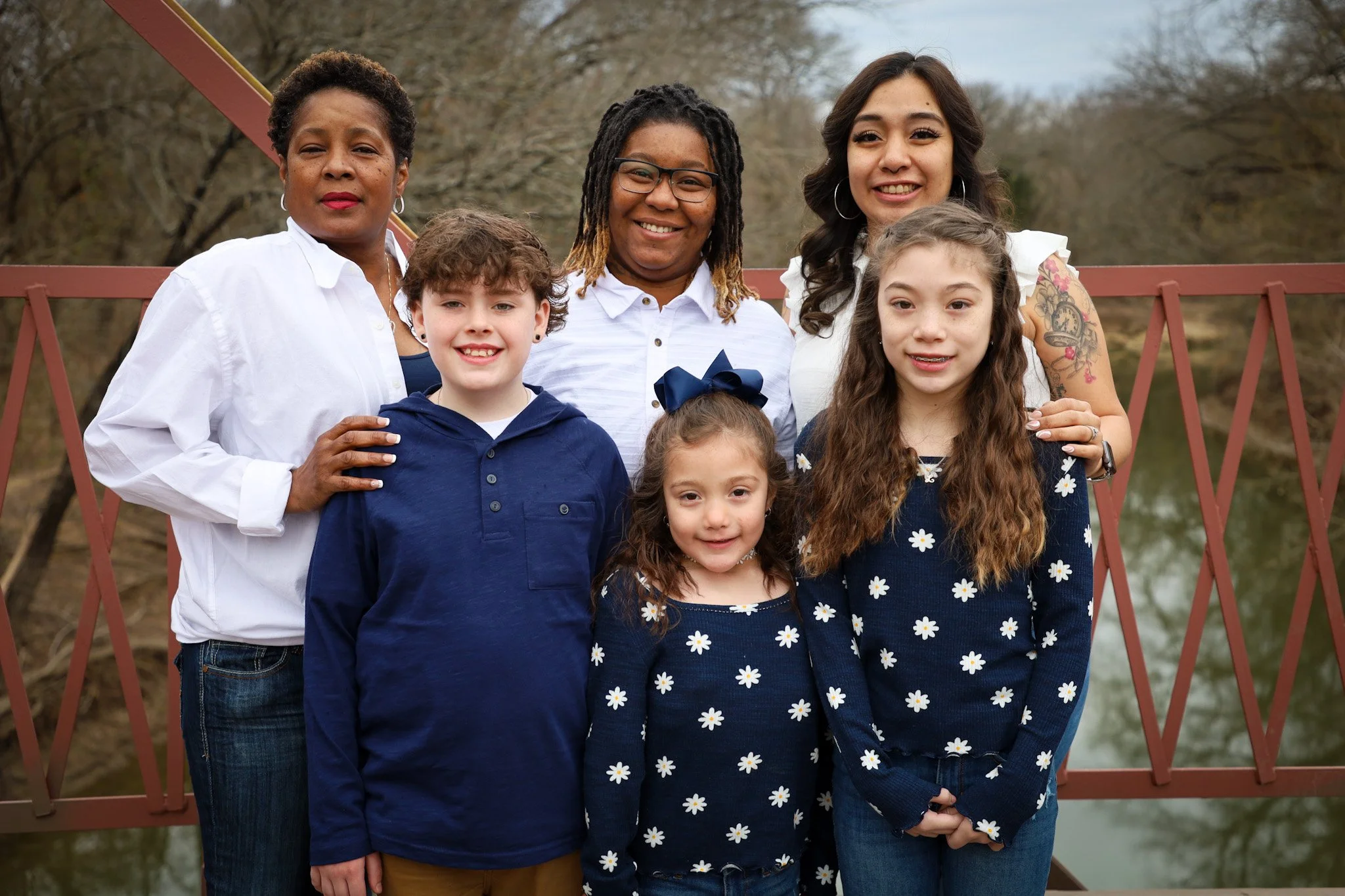 Group of women and children standing on a red bridge outdoors, smiling for the camera.