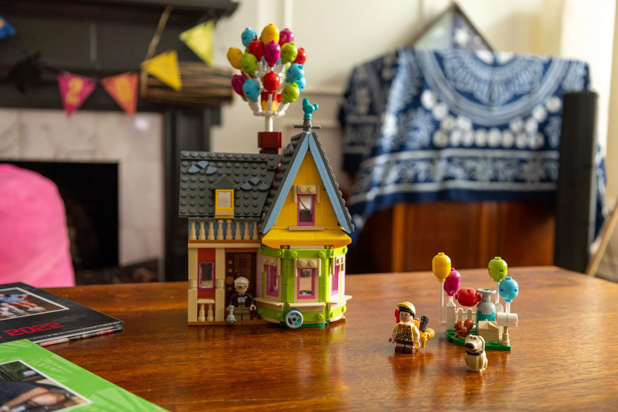 Colorful LEGO house with a yard, featuring several LEGO minifigures and a balloon bouquet on a wooden table.