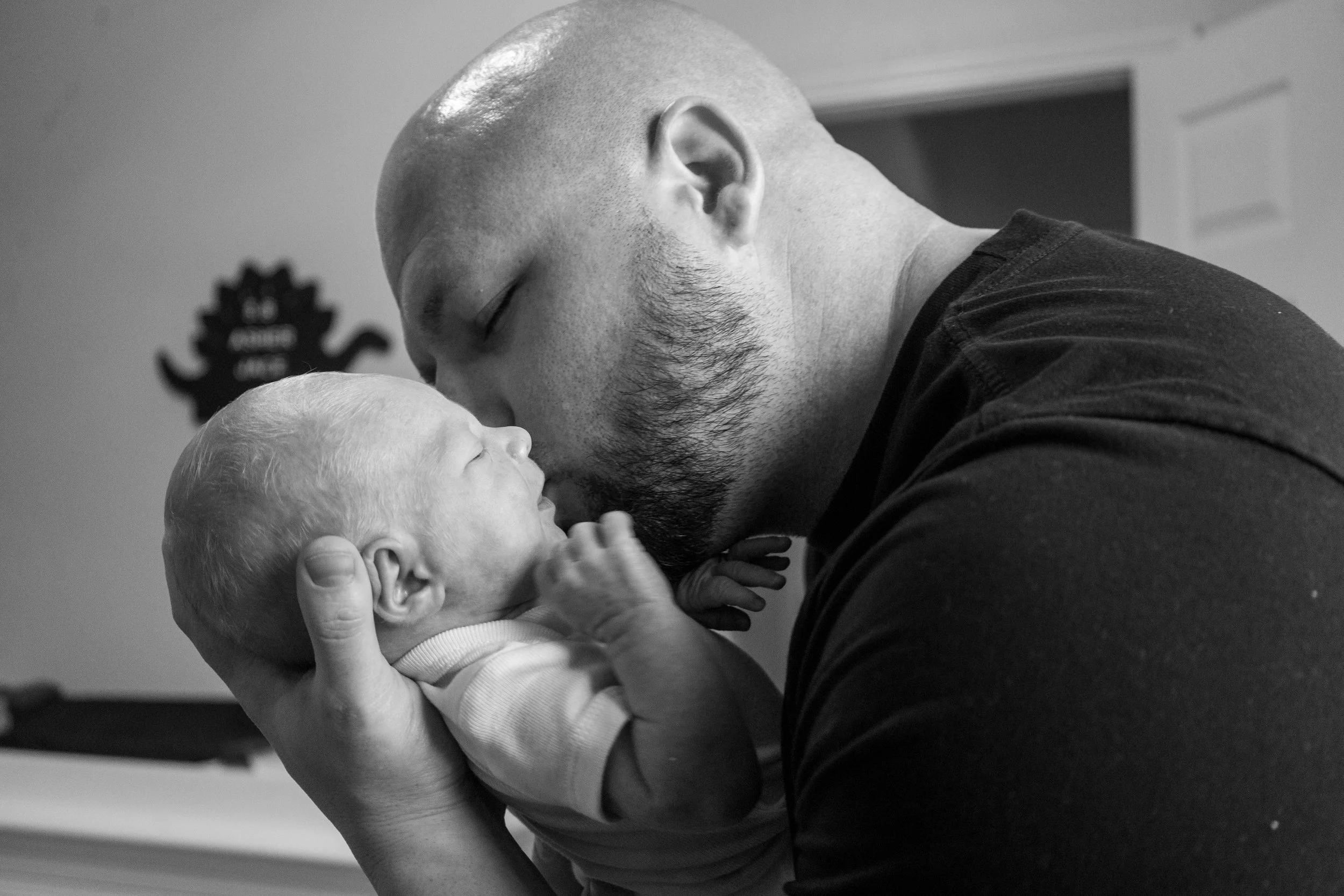 A man with a beard holds a newborn baby close, touching foreheads in a tender moment.