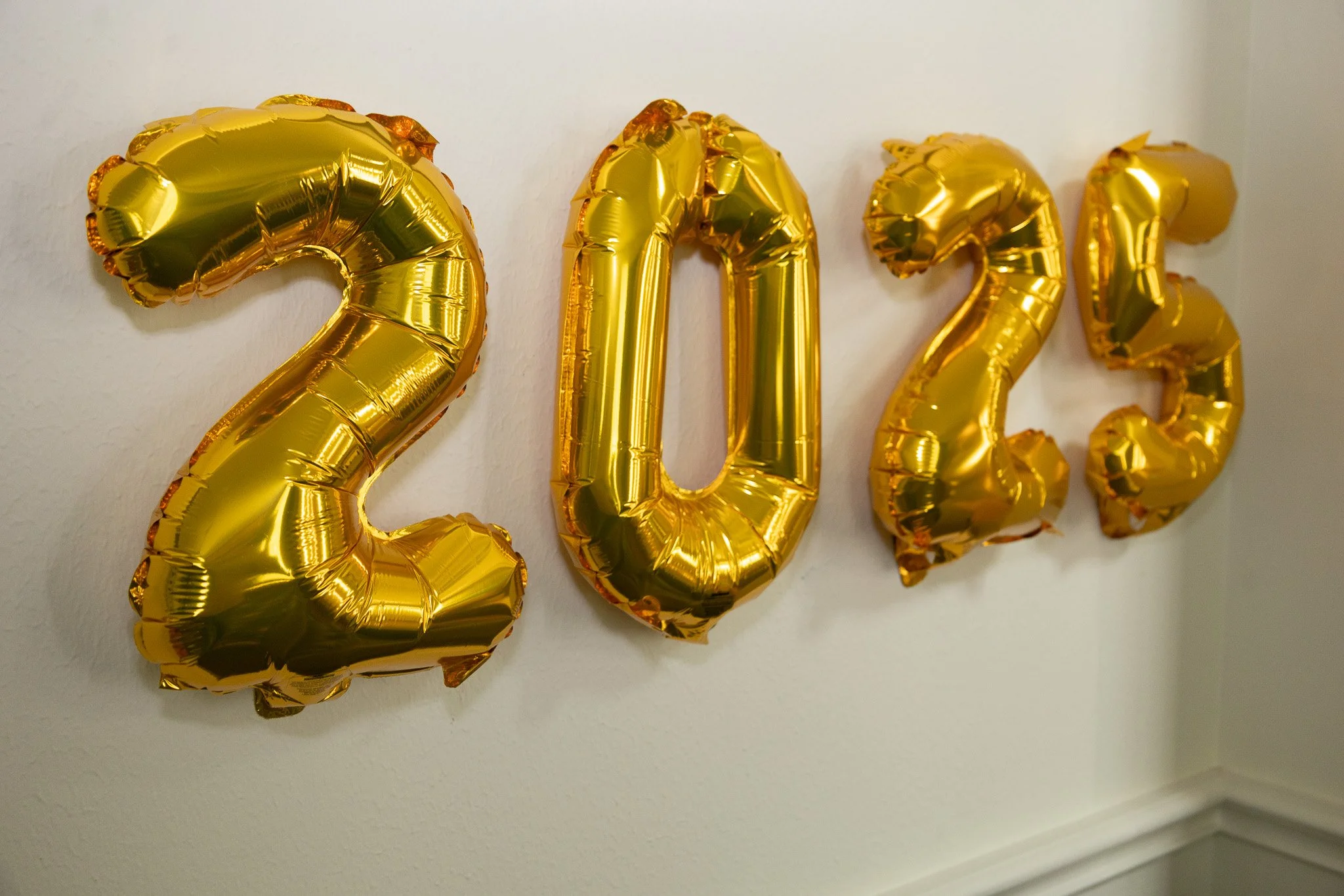 Gold foil number balloons forming '2023' on a white wall.