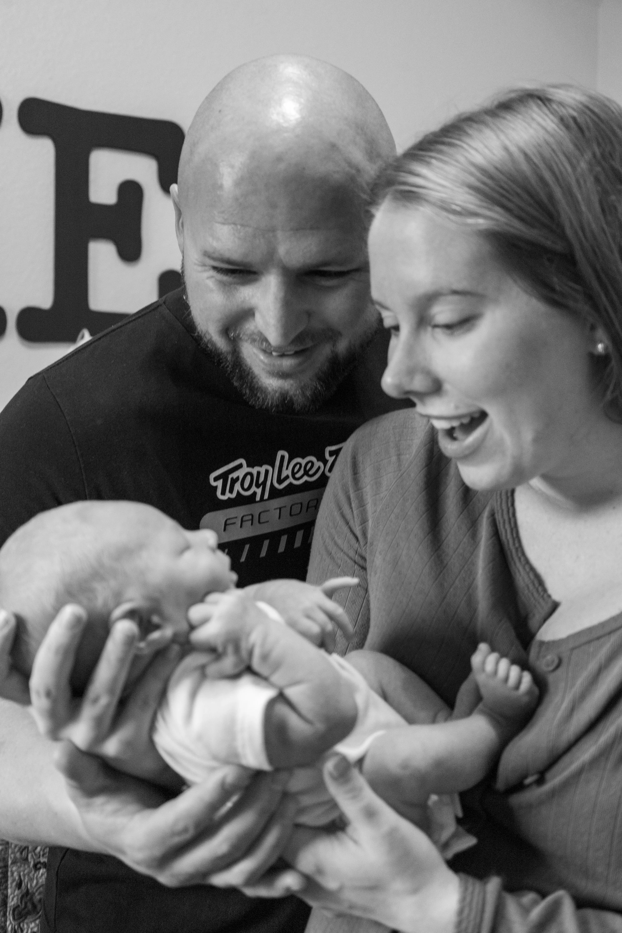 A couple holding a newborn baby in a hospital room, with the woman smiling and the man looking on affectionately.