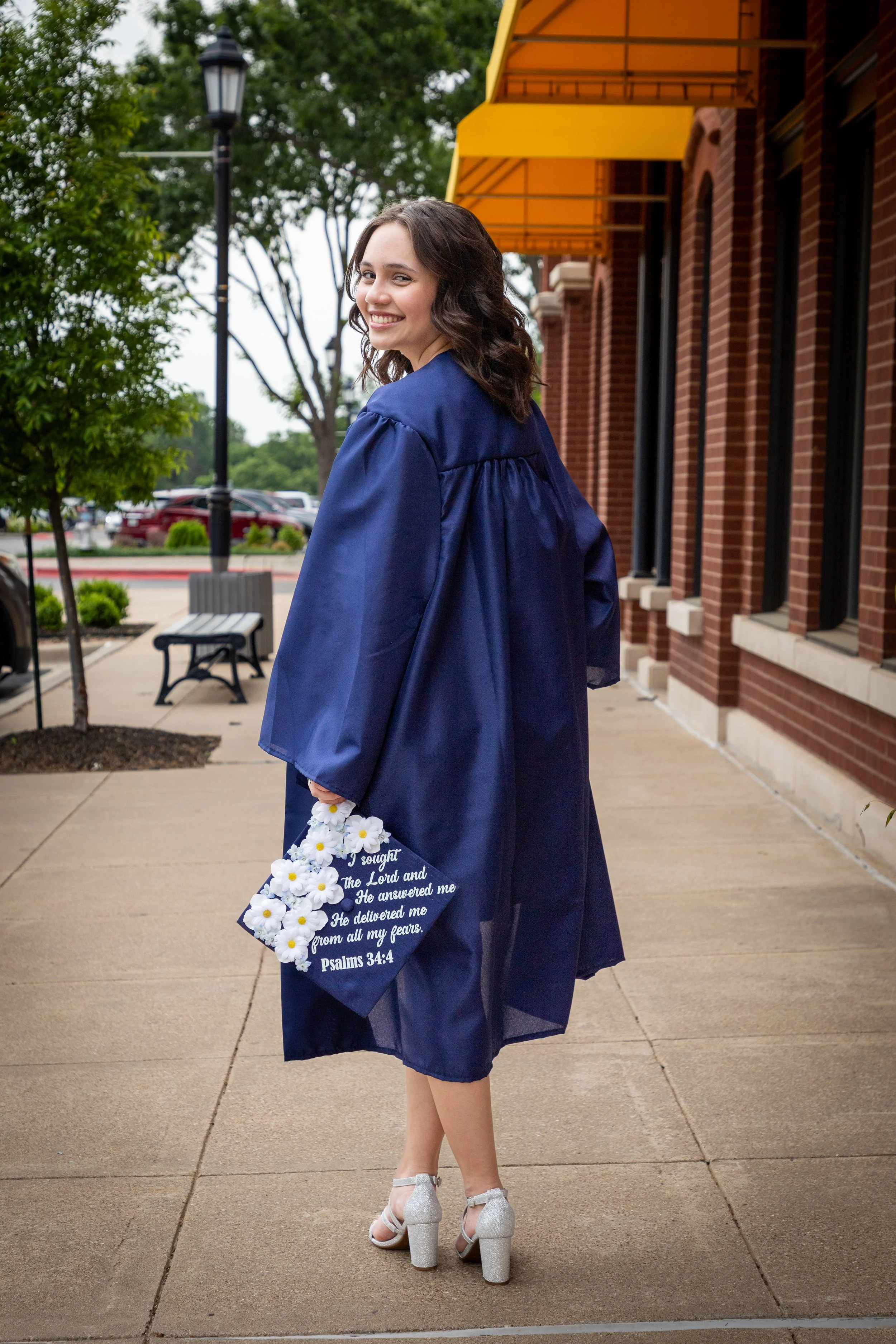 A young woman in a blue graduation gown smiling and holding a bouquet of white flowers with a quote from Psalms 34:4