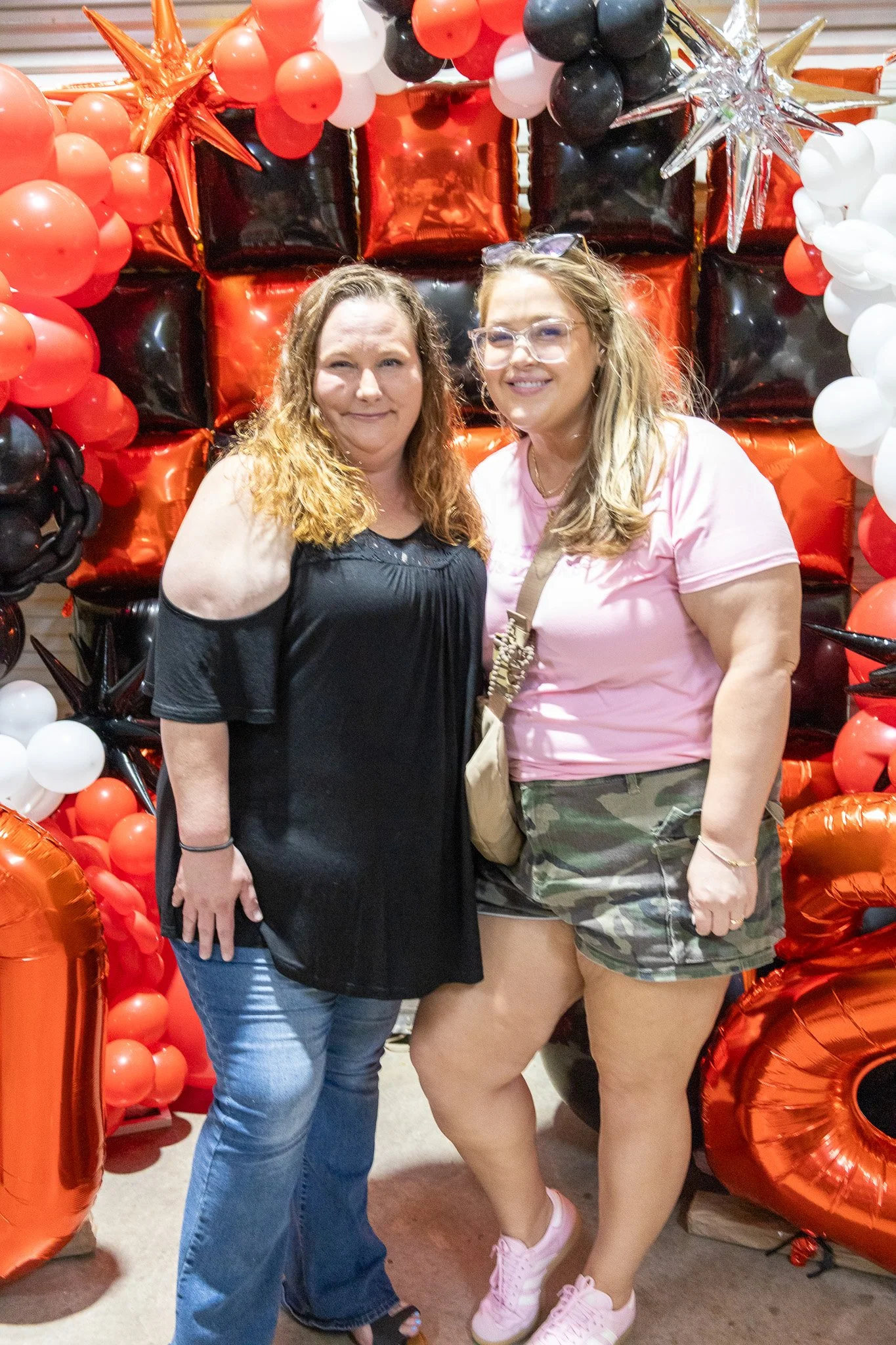 Two women standing in front of a large balloon display with red, black, and white balloons arranged as gift boxes, stars, and other shapes.