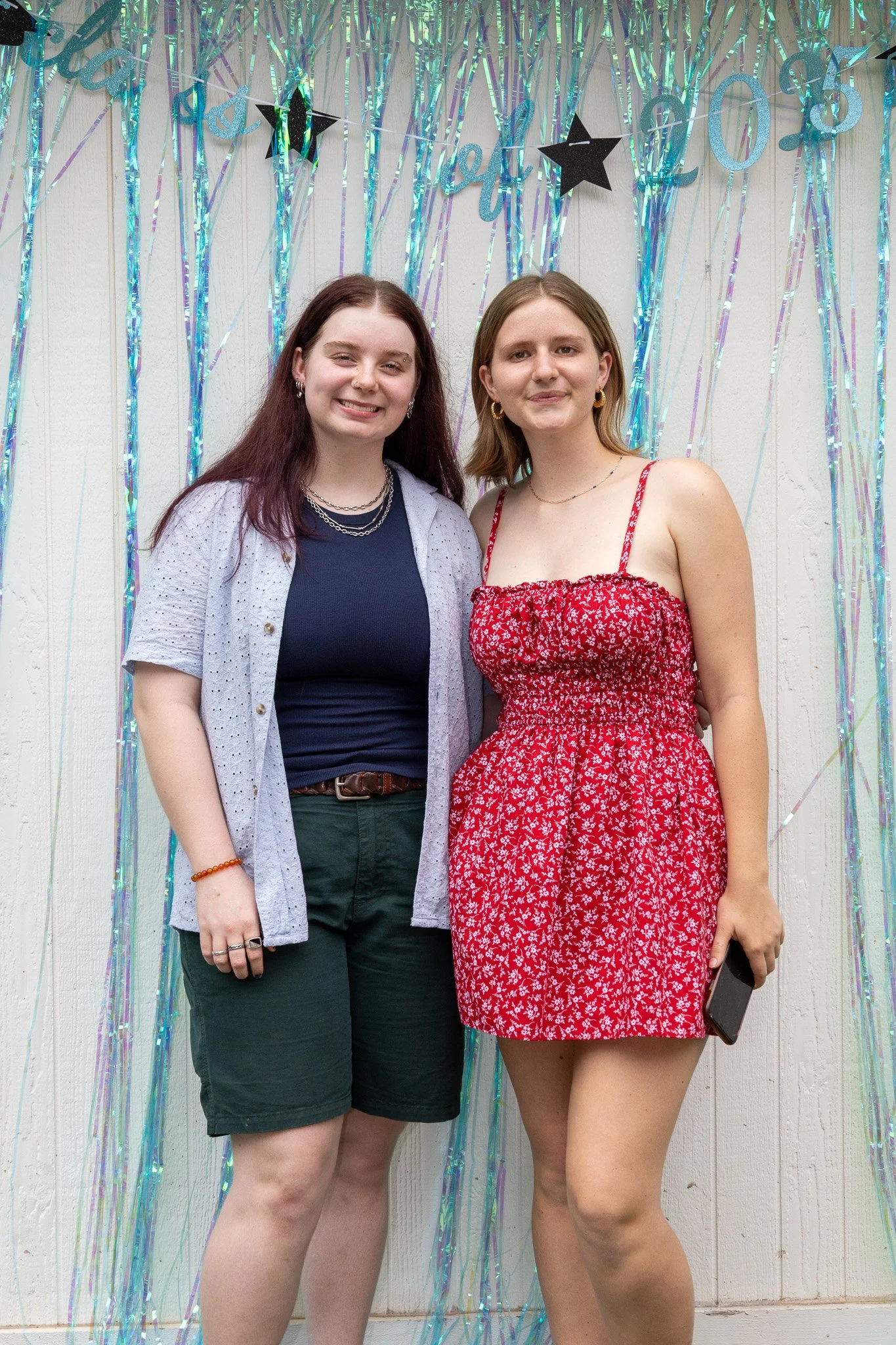 Two young women standing together in front of a decorative backdrop with blue and purple streamers and black stars, smiling at the camera.