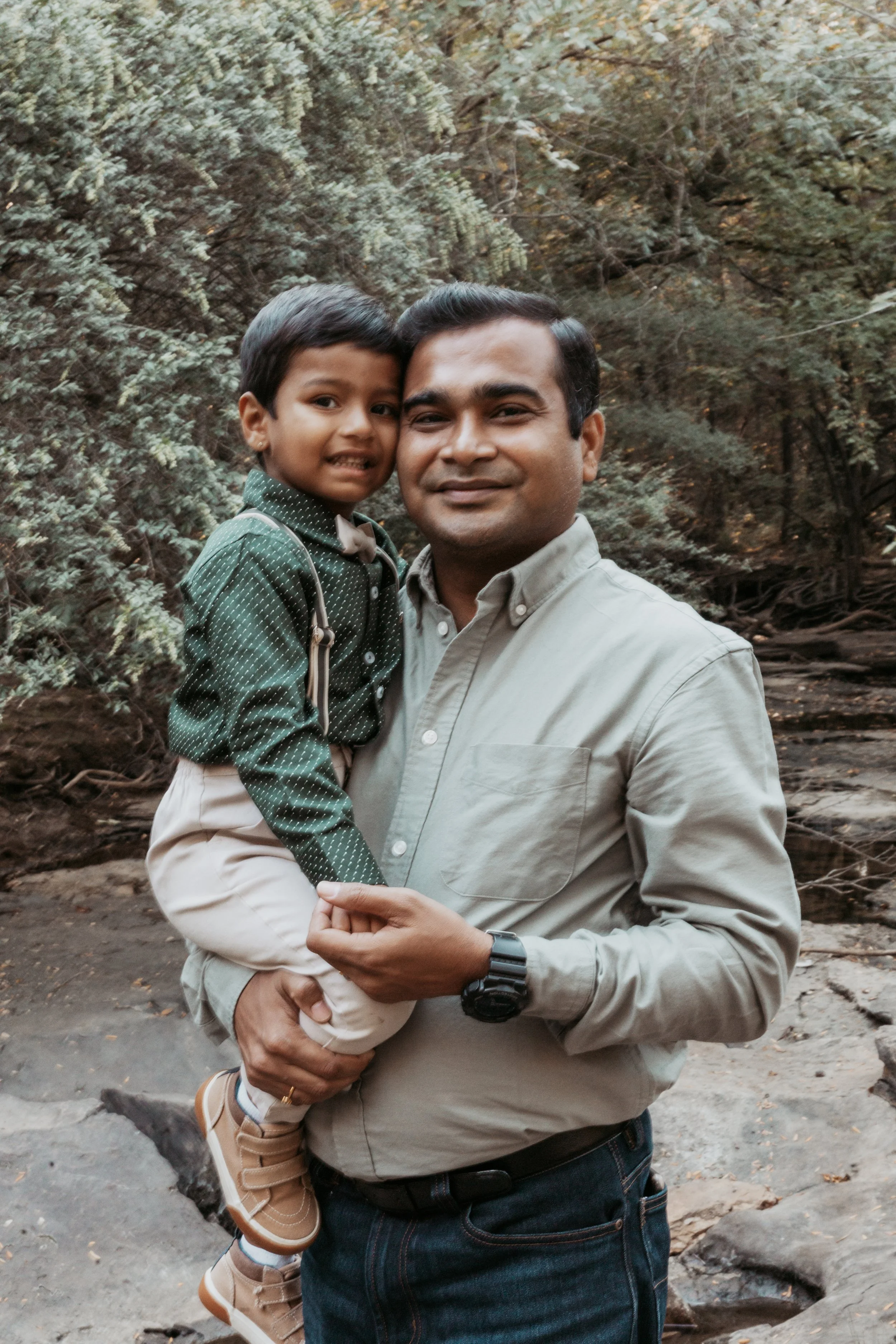 A man holding a young boy in a wooded outdoor setting.