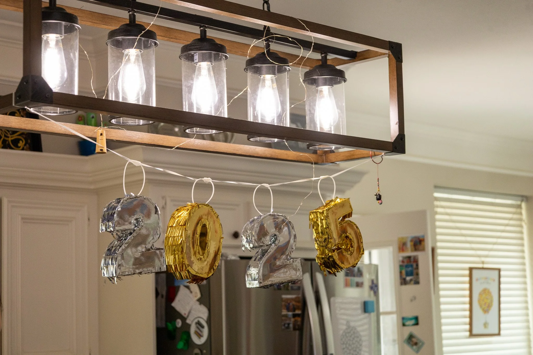 Decorations for New Year's 2022, featuring metallic balloons shaped as '2022' and gold '2025', with a ceiling light fixture with six exposed bulbs hanging above.