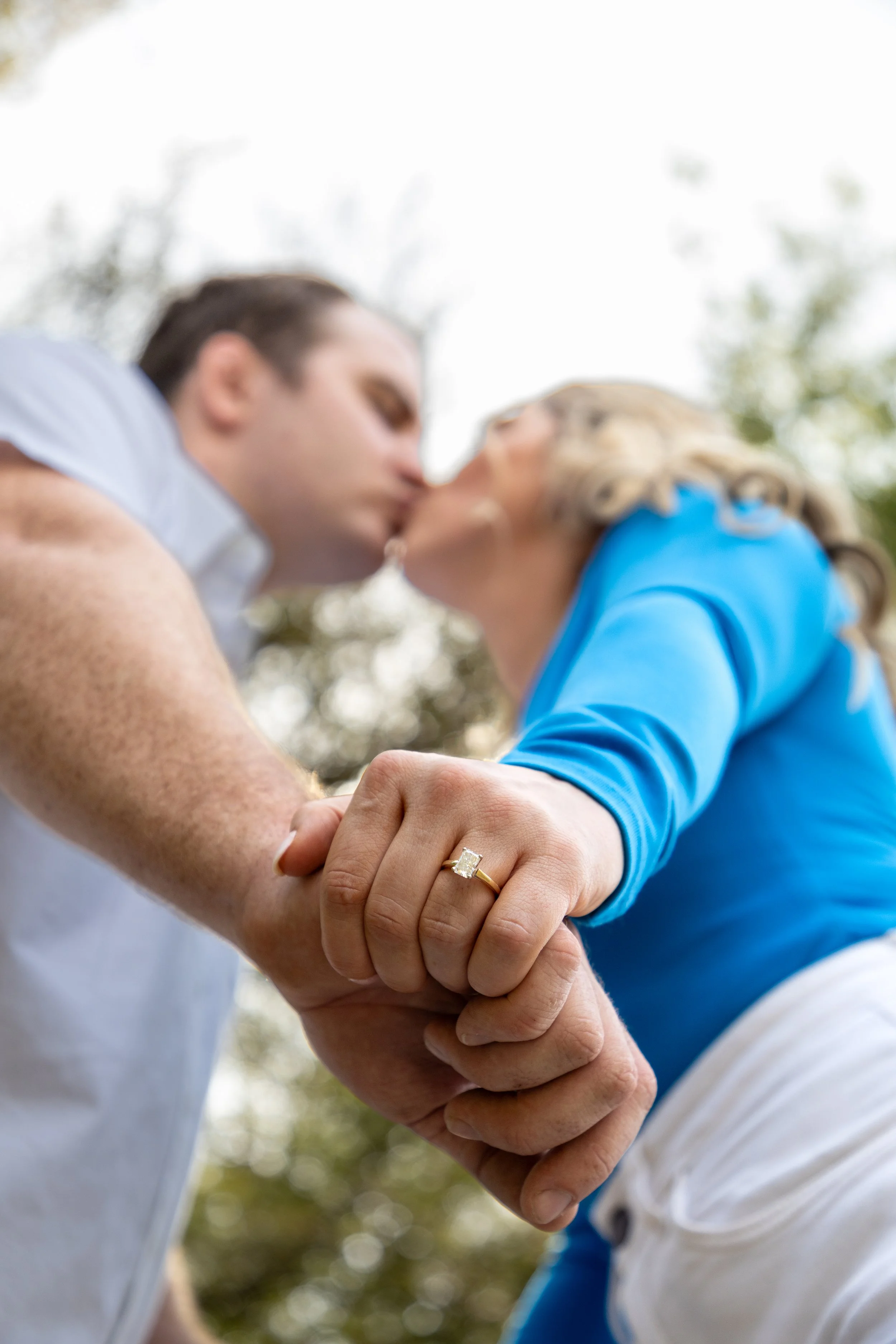 Close-up of a couple holding hands and sharing a kiss, with a focus on a gold ring with a diamond on the woman's finger.