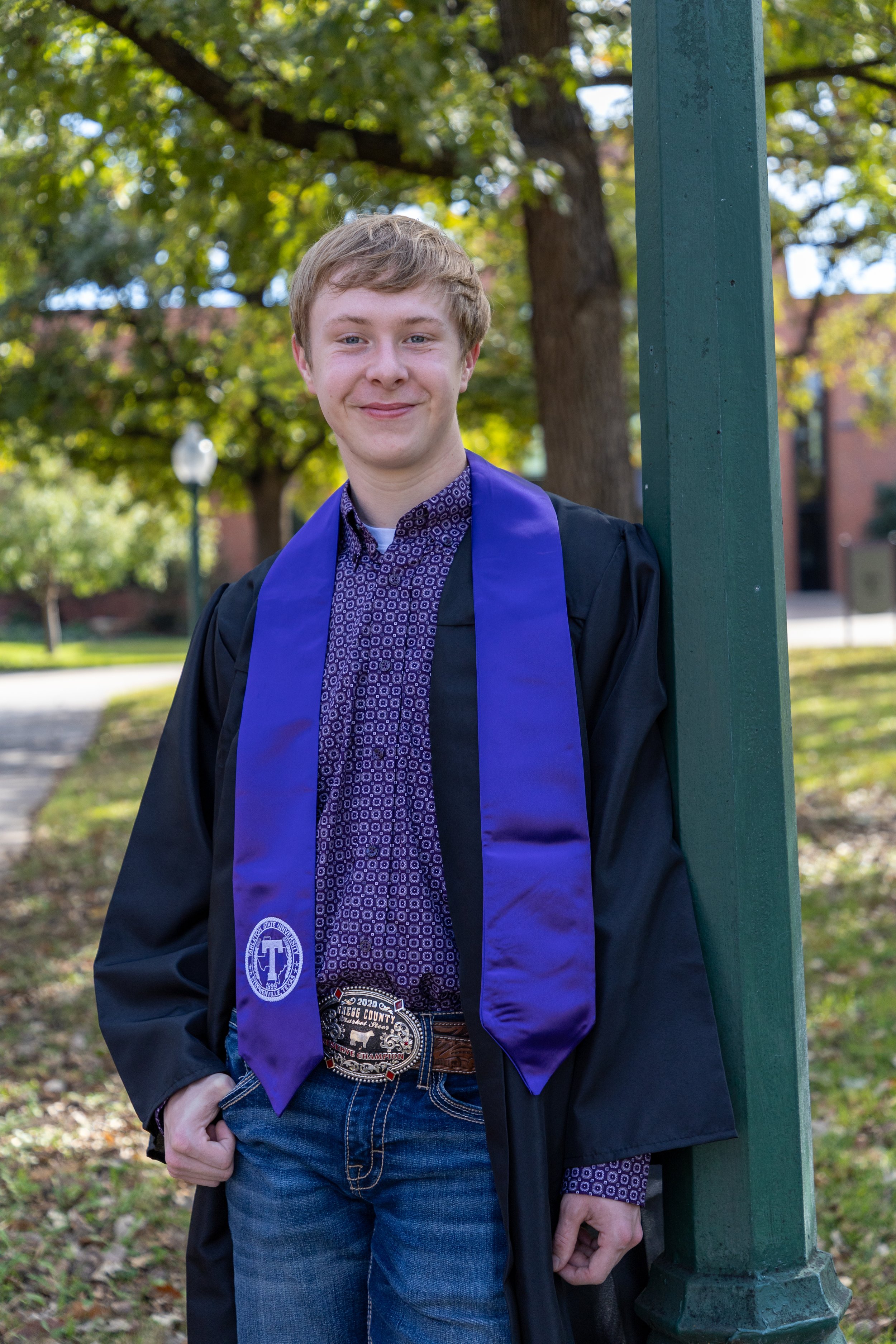 Young man in a graduation gown and purple stole standing outdoors,