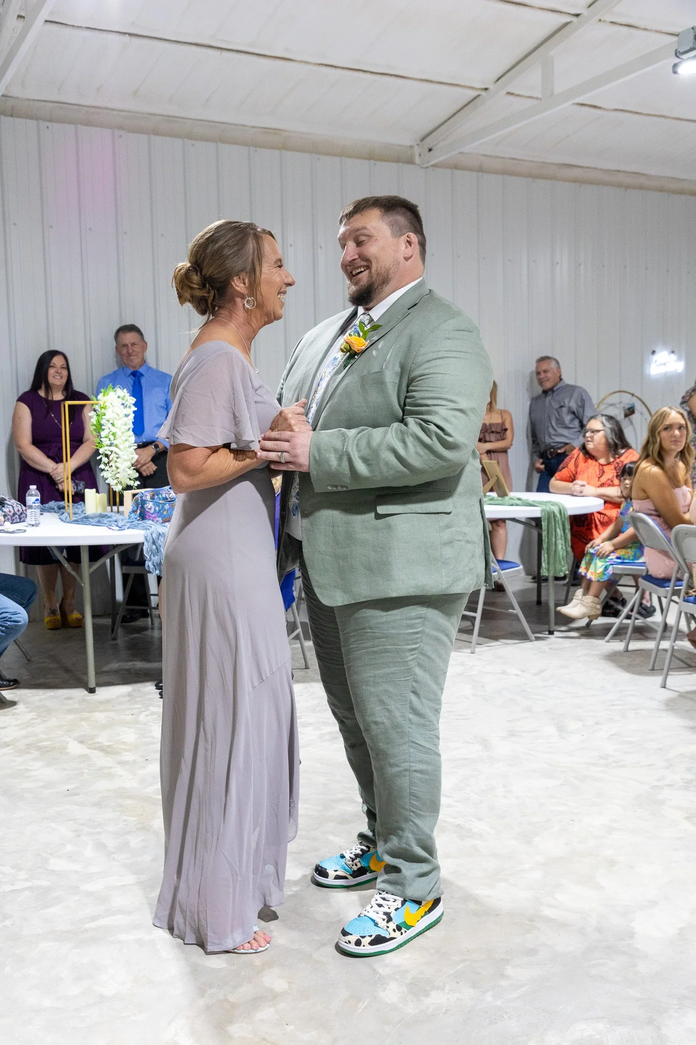 A woman and a man share a dance at an indoor celebration, with seated guests watching in the background.