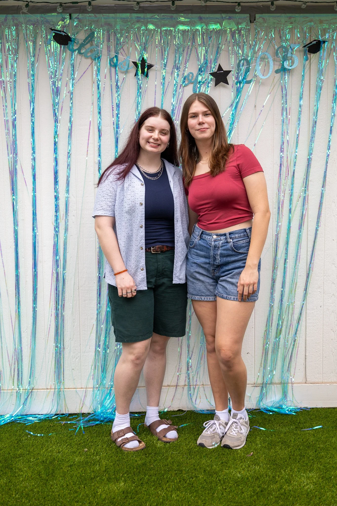 Two young women standing together in front of a shiny, decorative backdrop with streamers and star and graduation-themed decorations, celebrating a graduation in 2023.