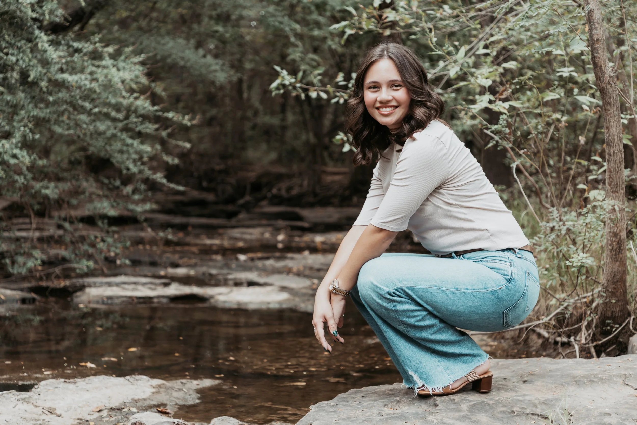 Smiling woman crouching by a creek in a wooded area
