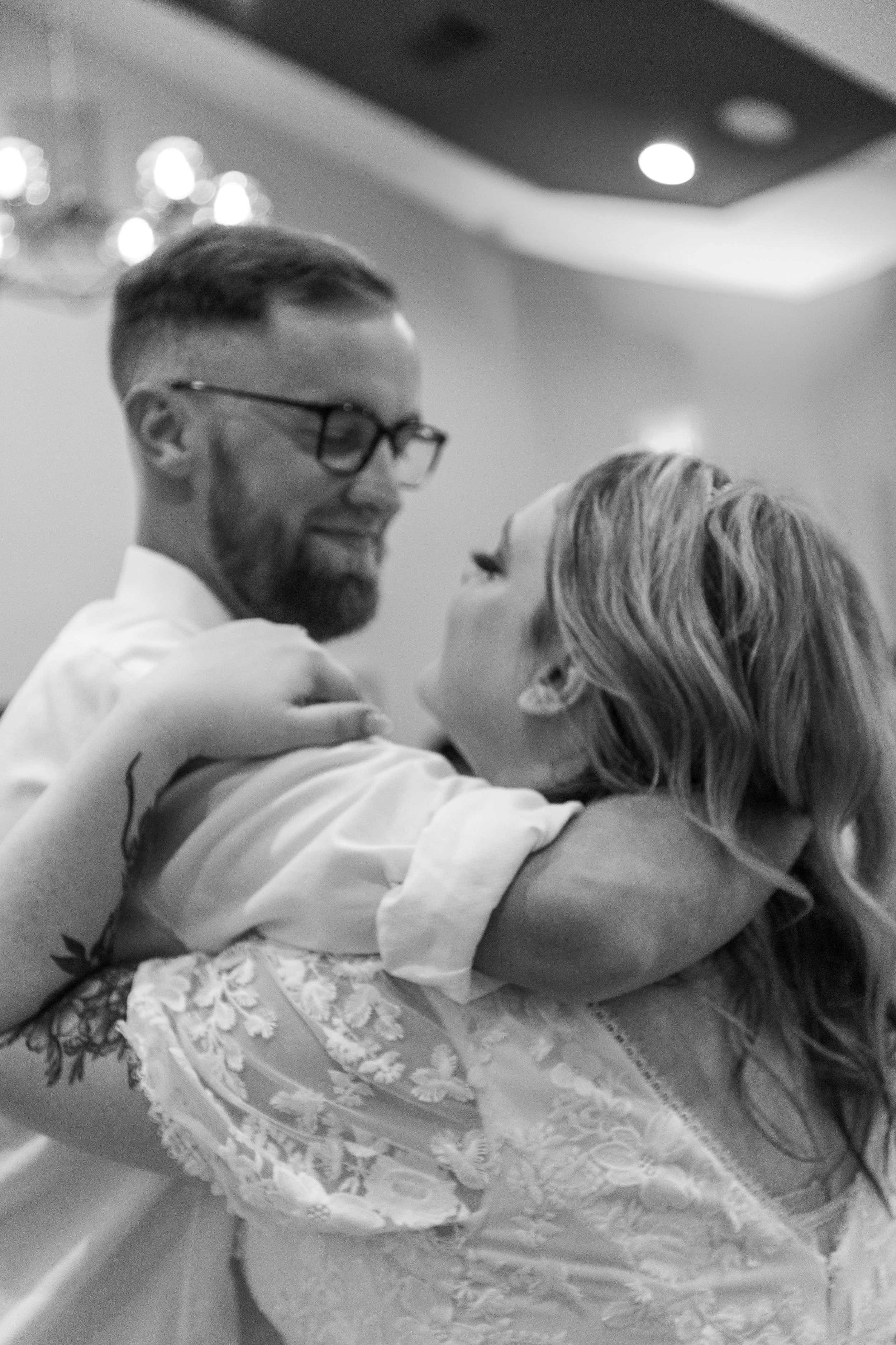 A couple hugging and dancing at a wedding reception, smiling at each other in a ballroom or banquet hall.