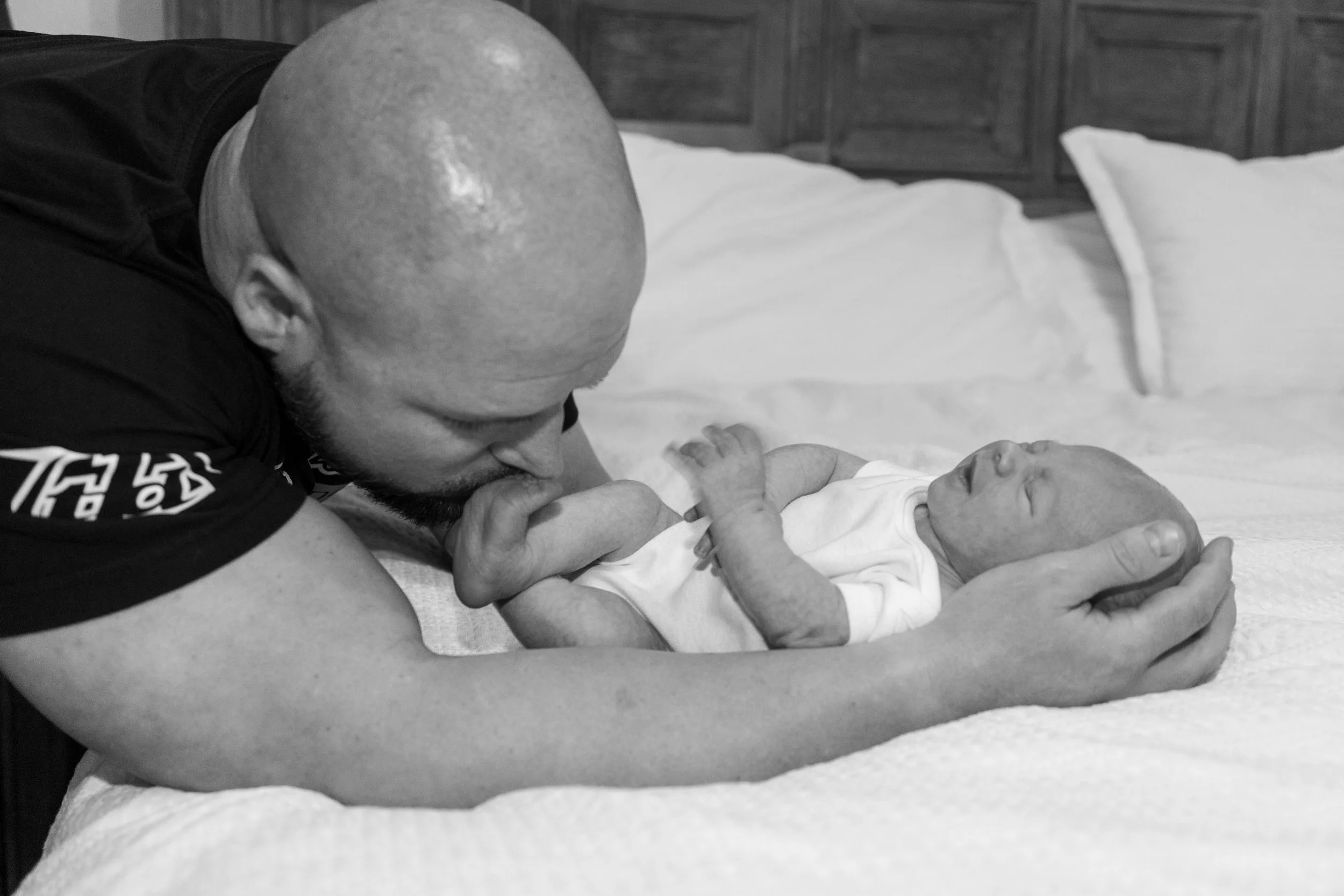 A man lying on a bed, gently touching a newborn baby on the face, in black and white.