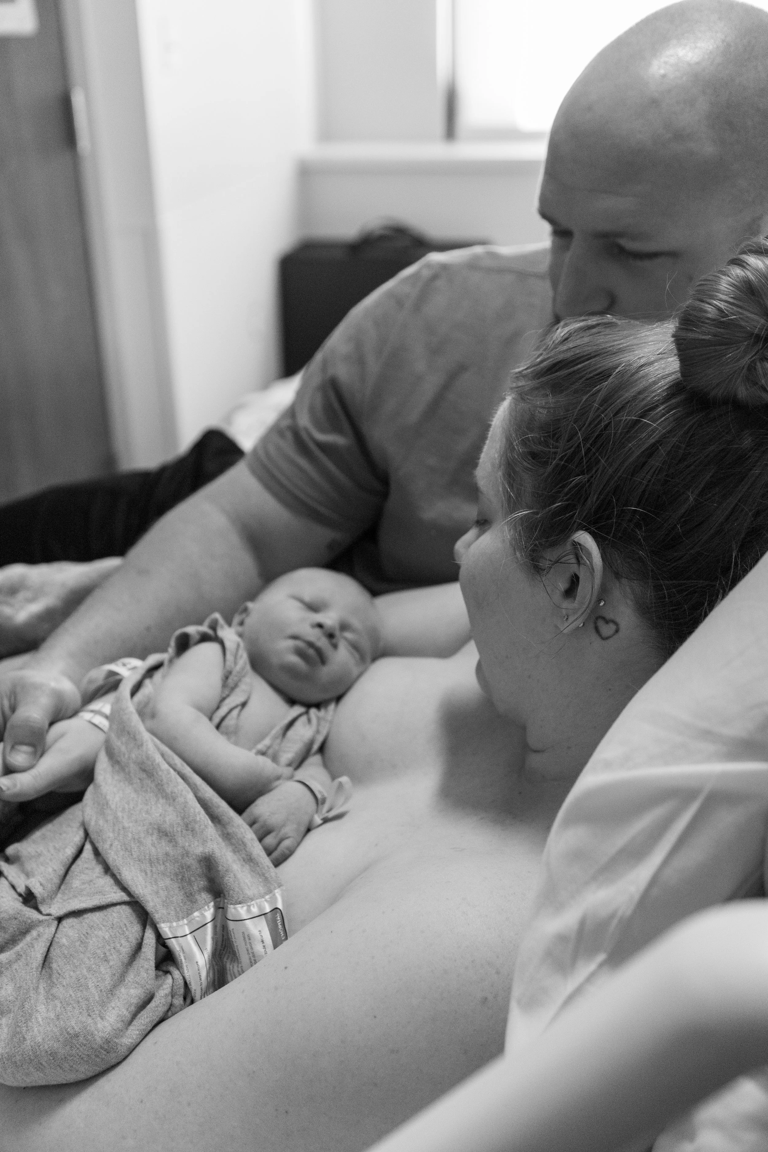 A family moments after a baby's birth, with the newborn lying on mother’s chest, father and mother looking at the baby in a hospital room.