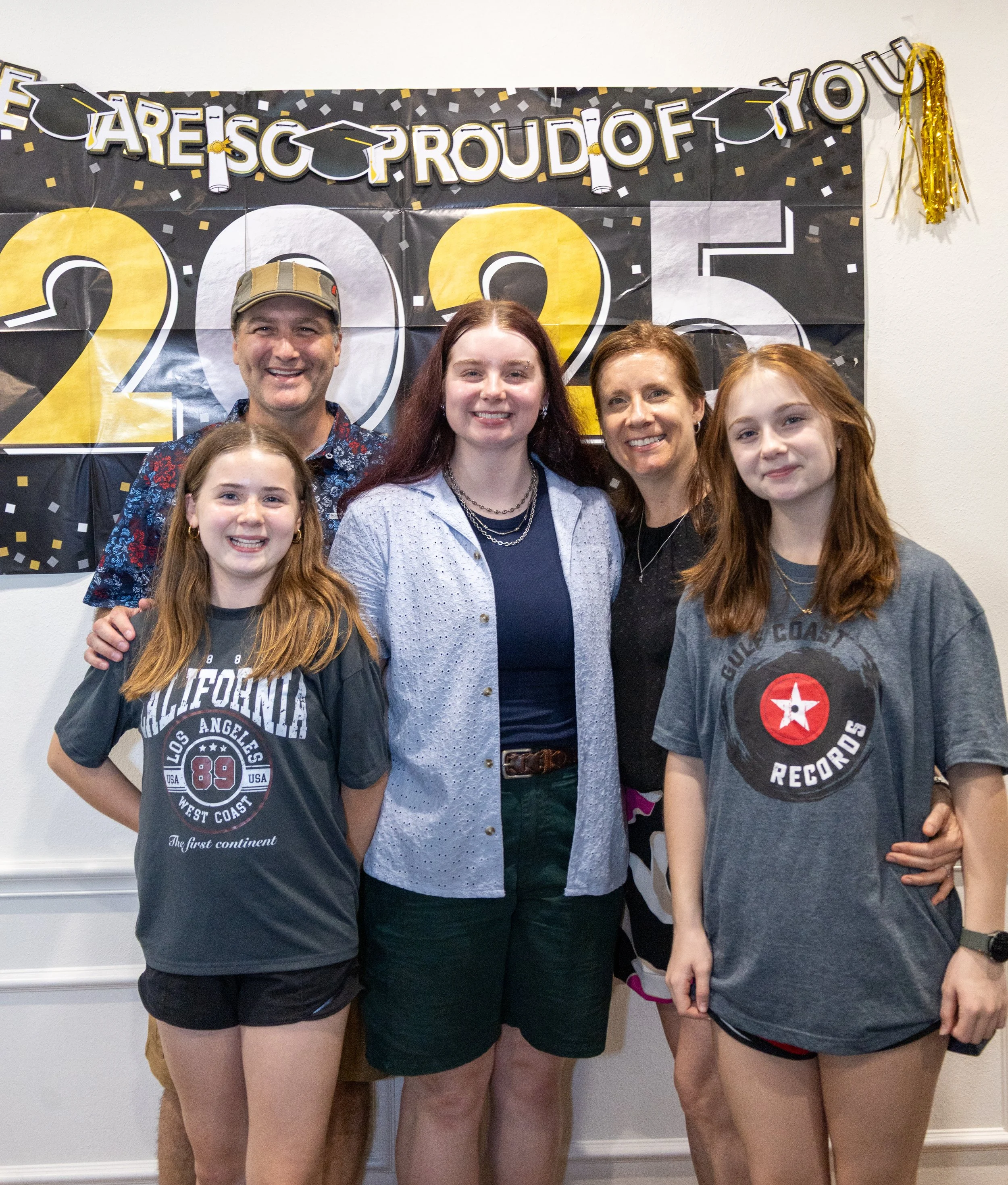 A group of five people smiling at a graduation celebration, standing in front of a black and gold '2023' banner with the words 'Are So Proud of You' at the top.