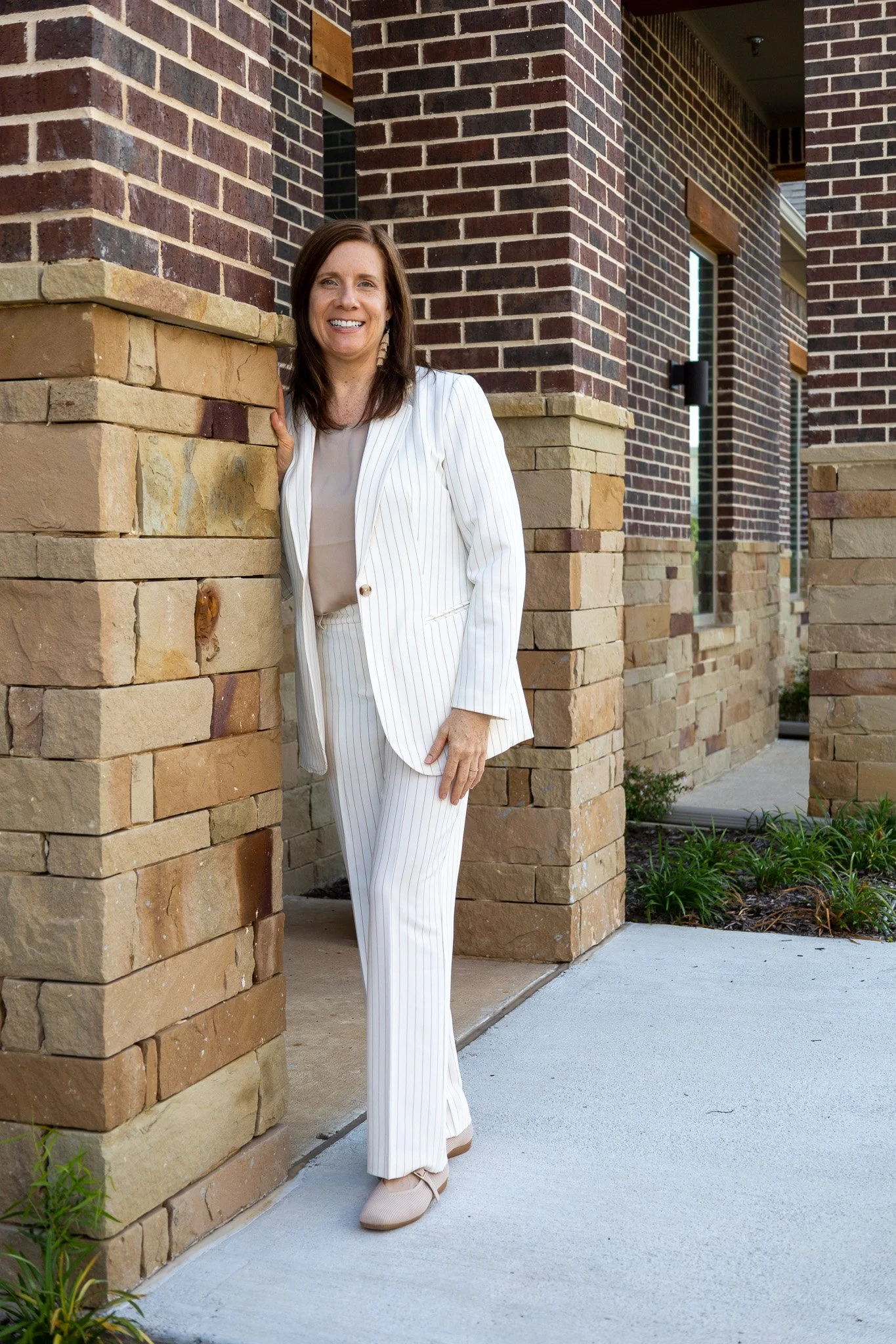 A woman in a white pinstripe suit standing outside a building with brick and stone walls, smiling at the camera.