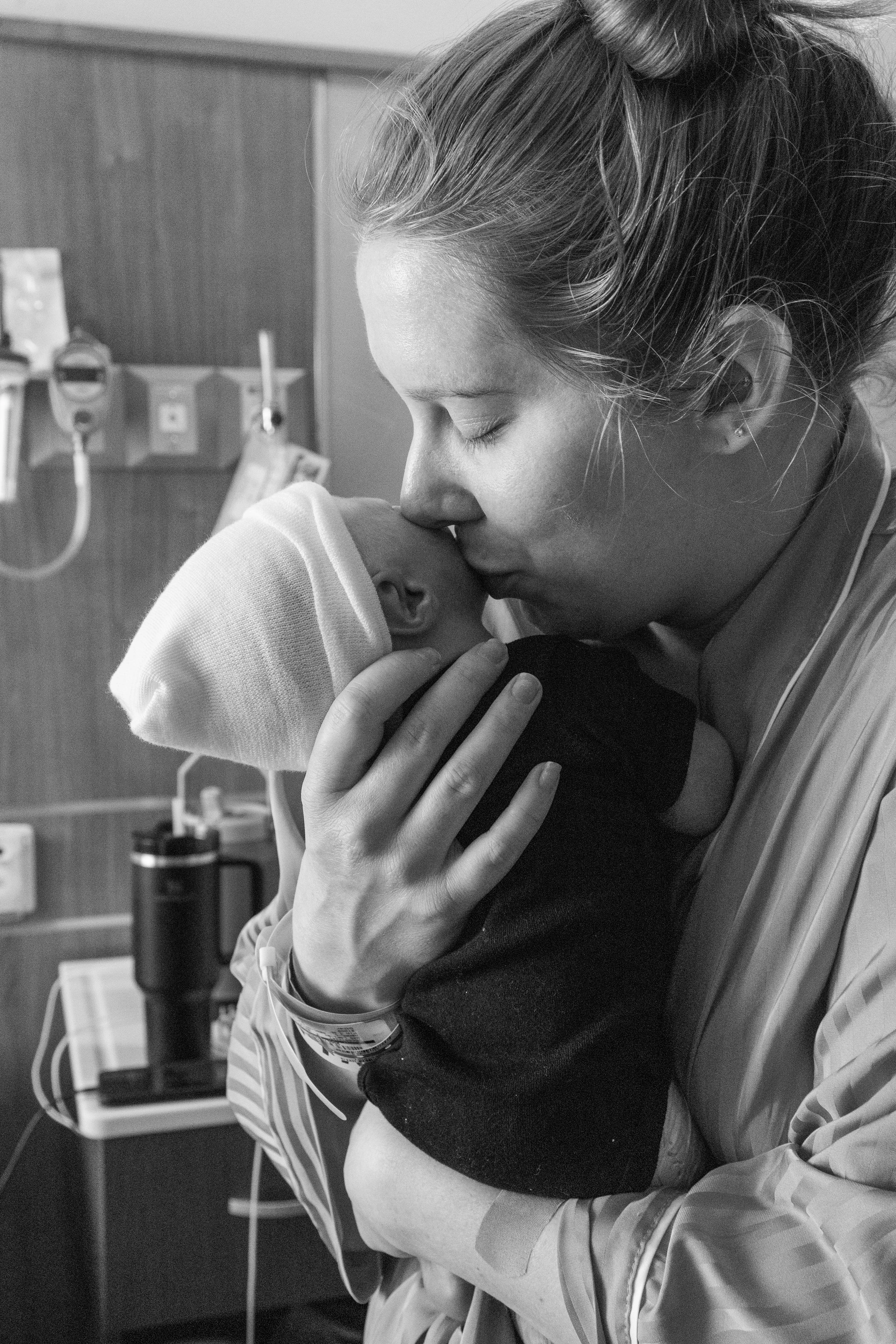 A woman in a hospital gown holding a newborn baby close, pressing her forehead to the baby's as they share a tender moment.