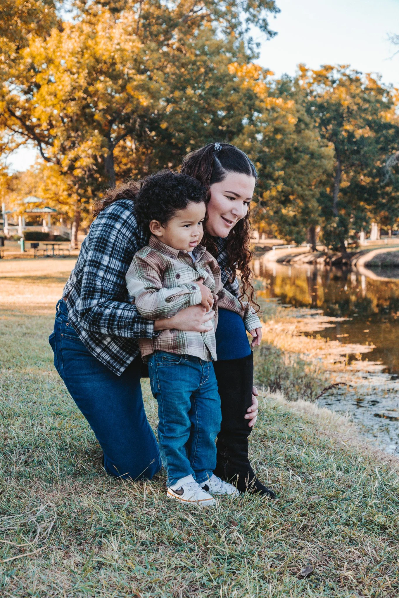 A woman and a young boy looking into a lake, surrounded by trees with autumn foliage.