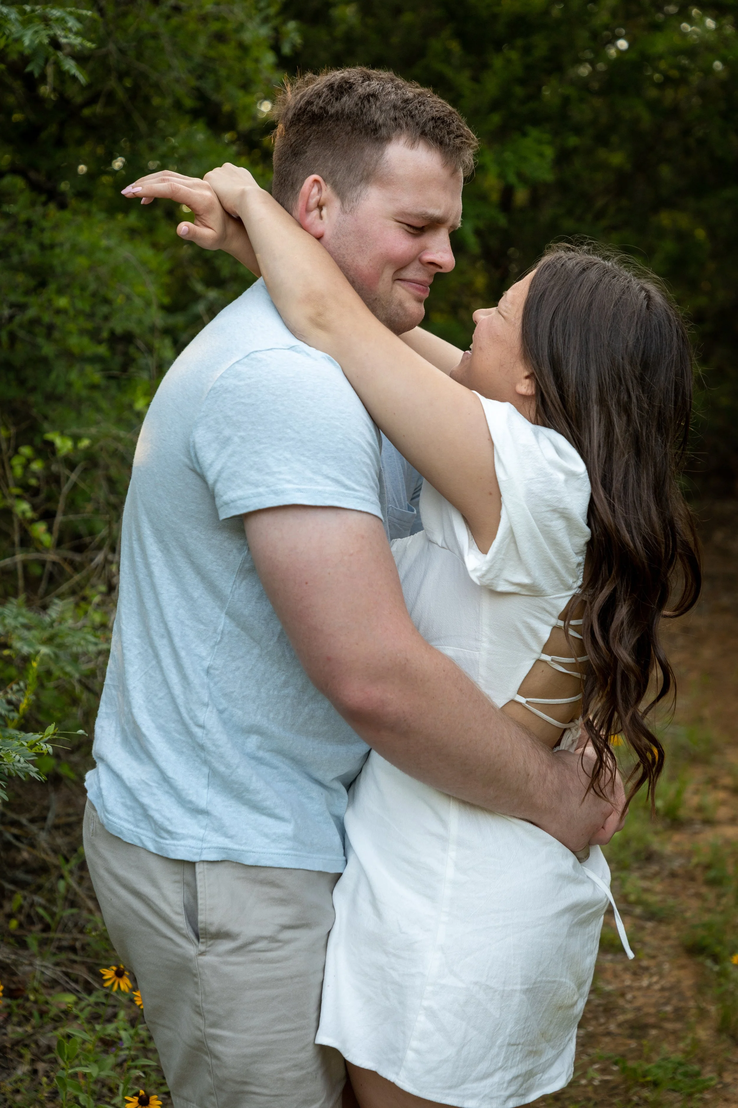 A couple sharing an emotional embrace outdoors surrounded by greenery.