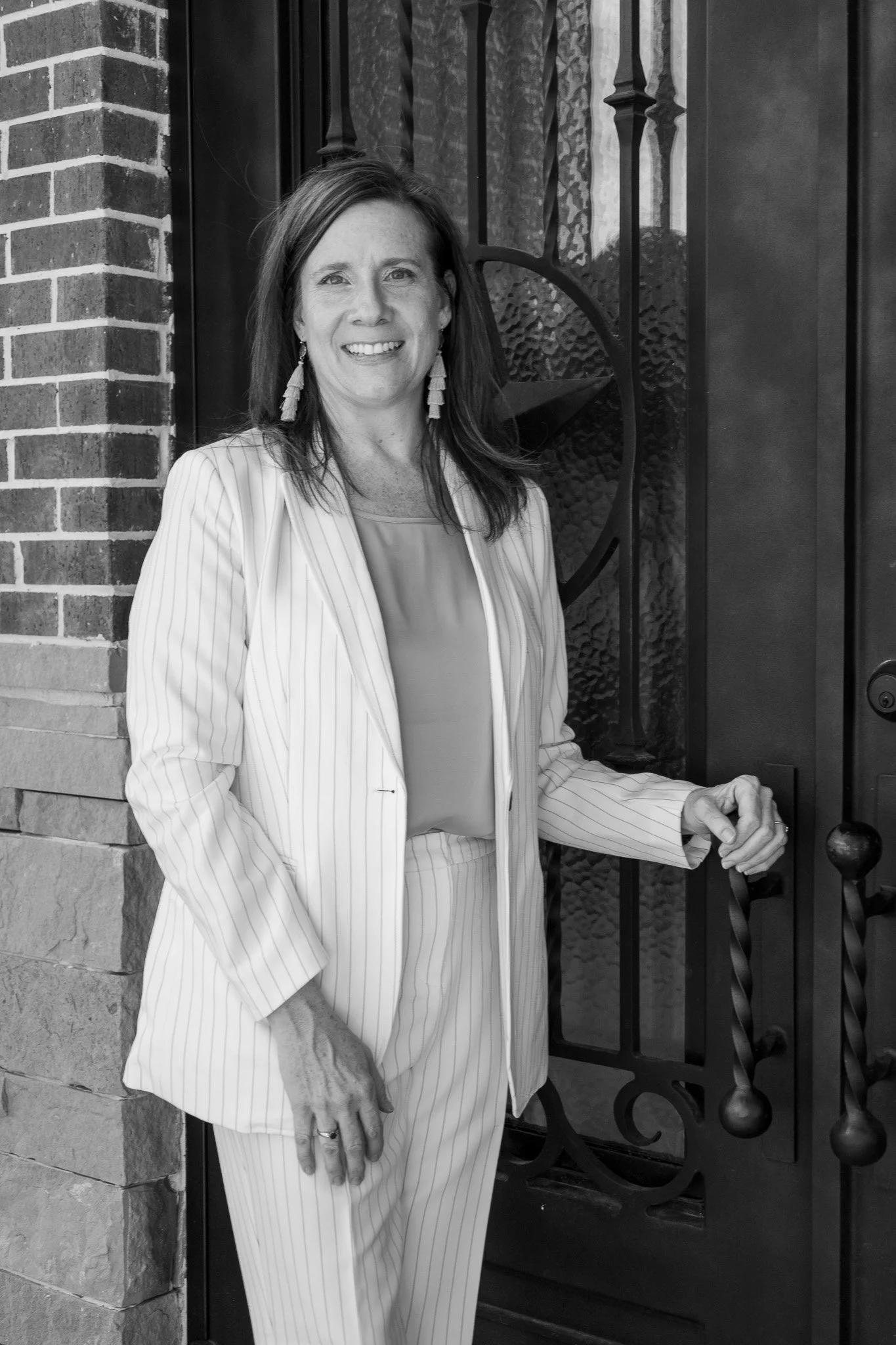 A woman in a light-colored, pinstripe suit standing outside by a black wrought iron gate, smiling at the camera.