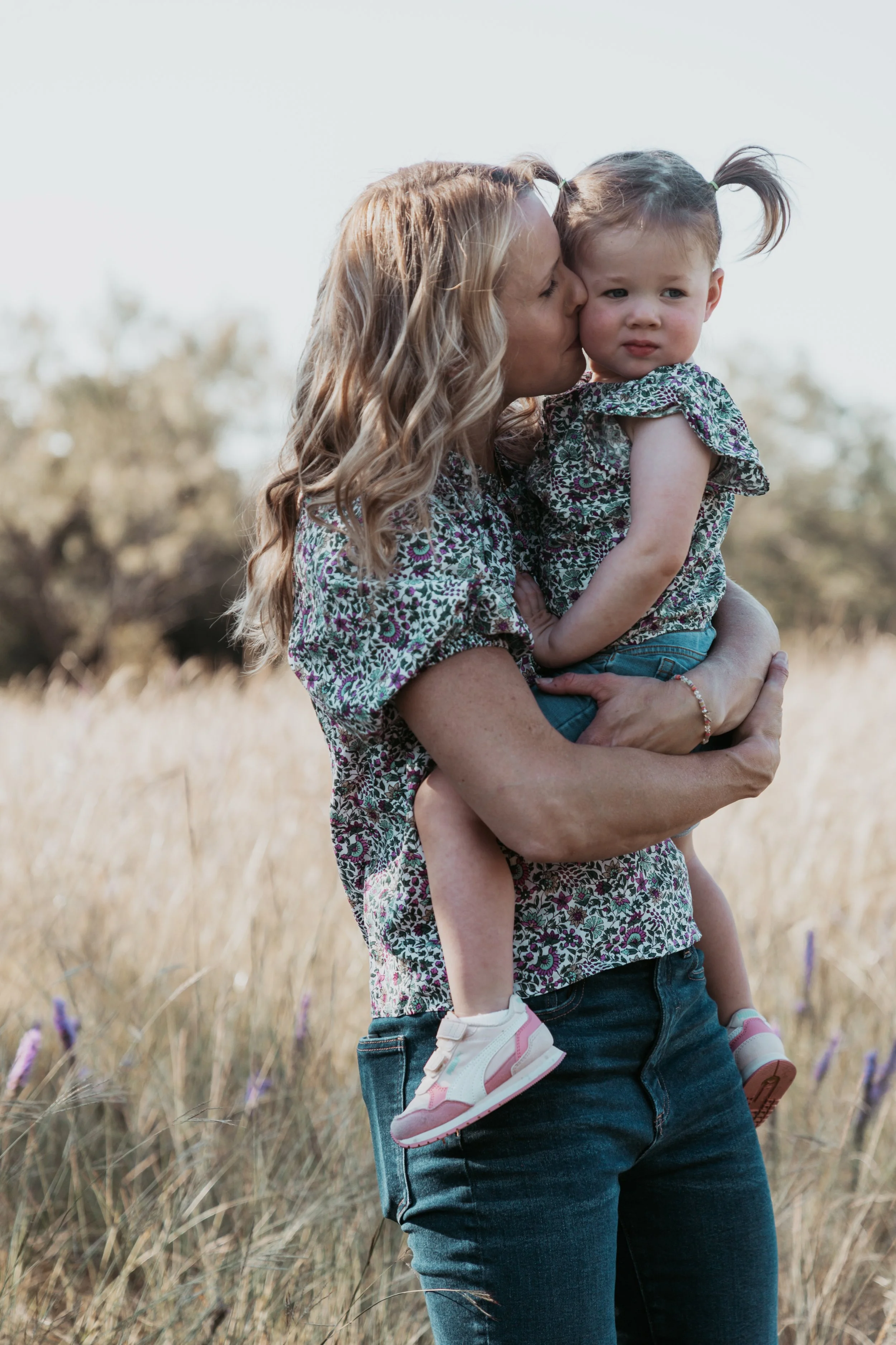 A woman holding a young girl in a field of tall grass with trees in the background