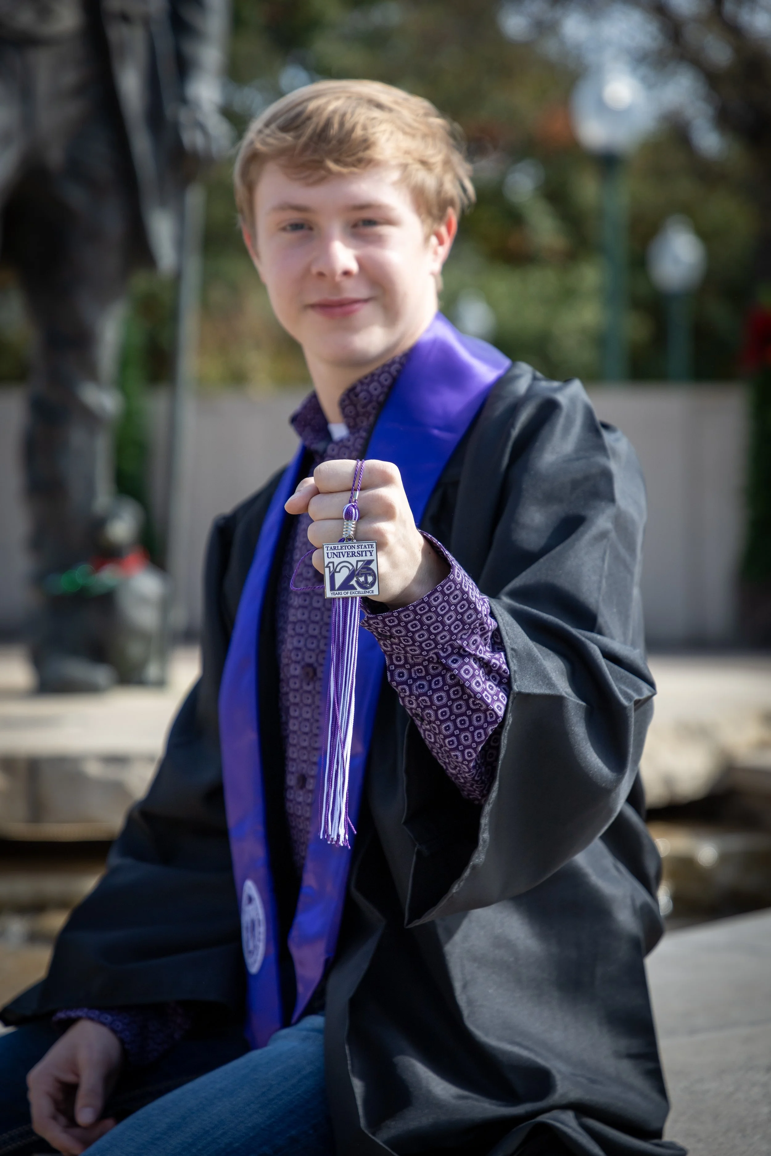 Young man in graduation gown showing his diploma and wearing a medal with the logo of Tarleton State University