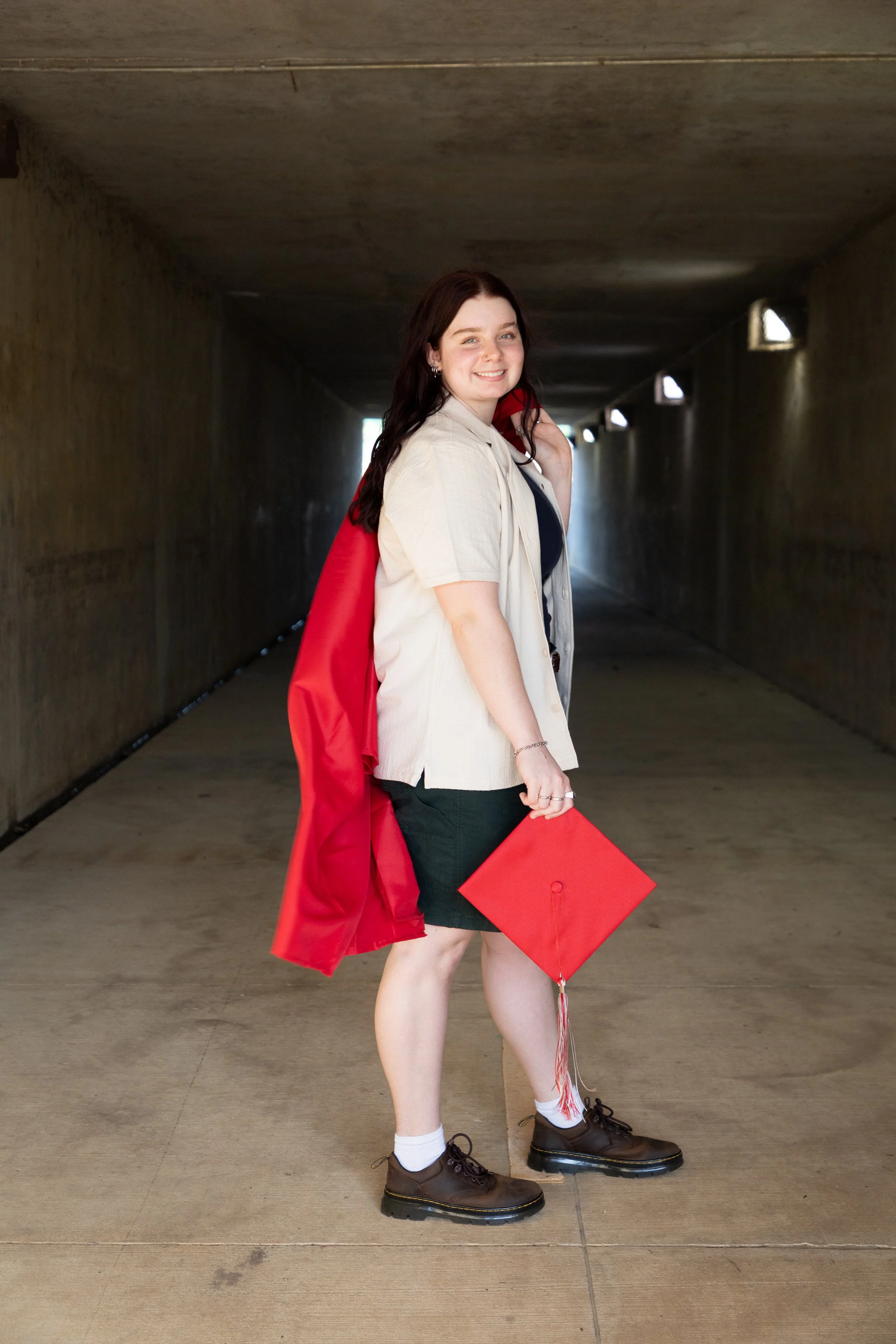 Young woman in graduation cap and gown holding diploma in underpass.