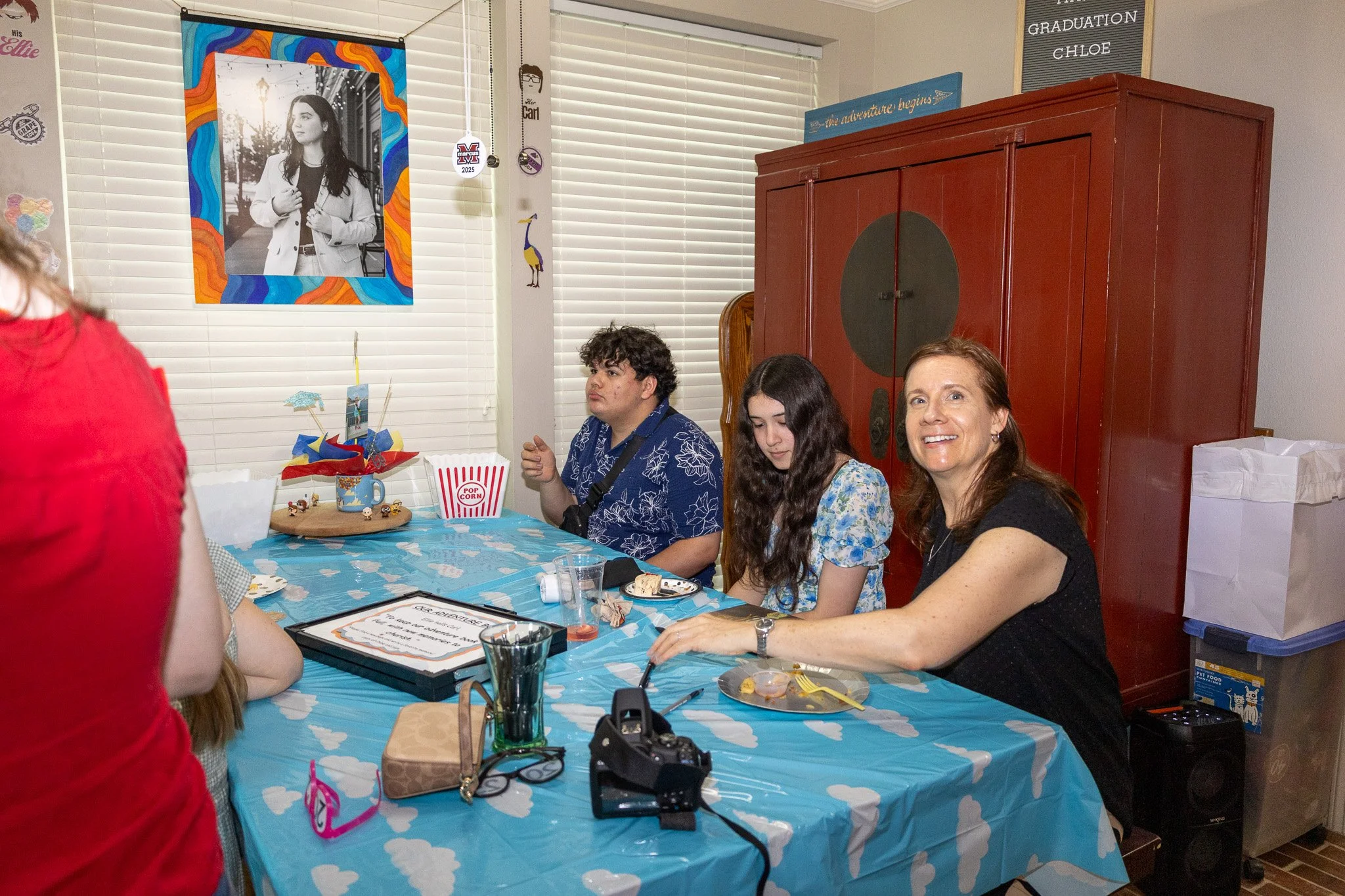 People sitting at a table celebrating a graduation, with a large red cabinet in the background and various decorations on the walls.