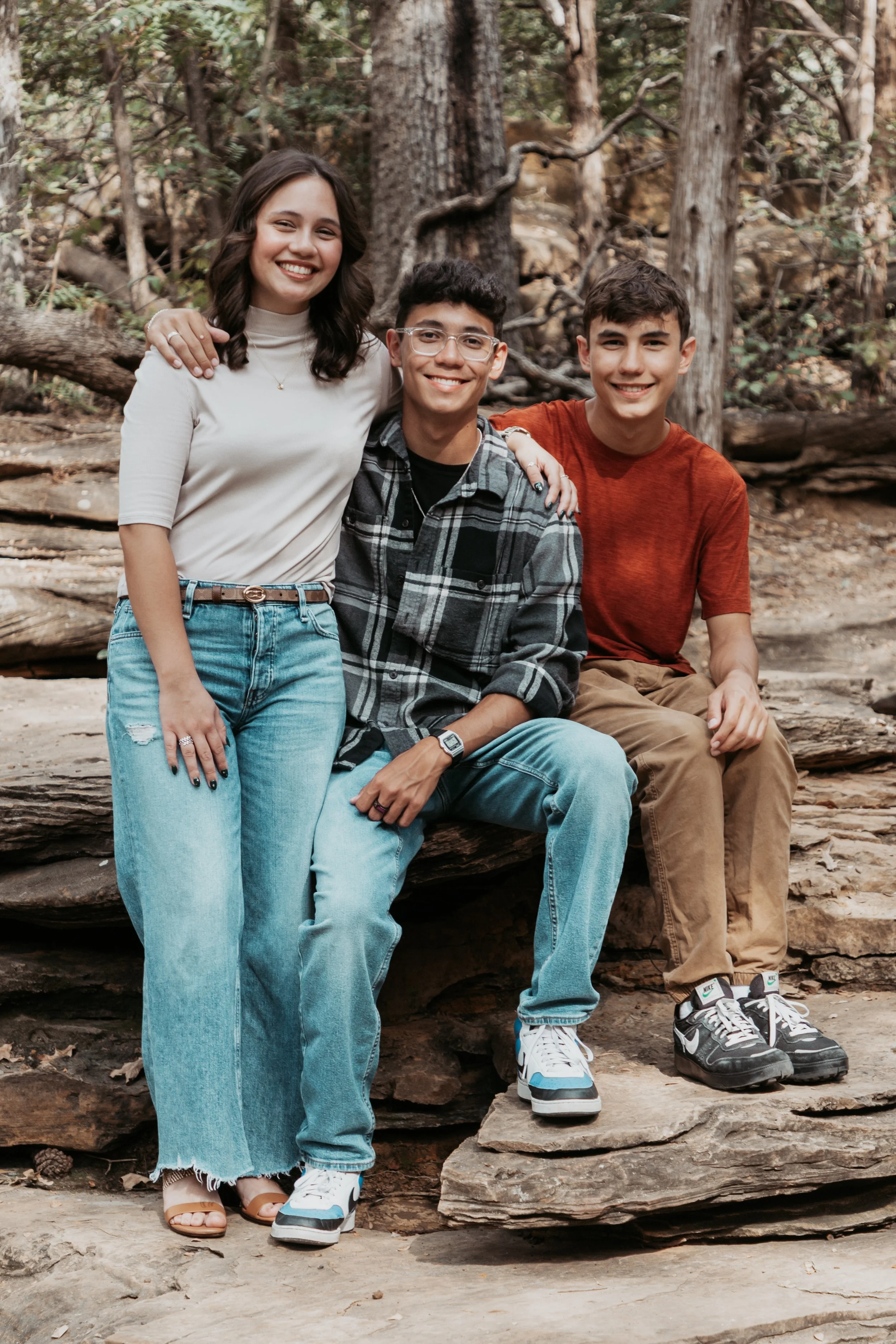 Three teenagers smiling and sitting on rocks in a forest.