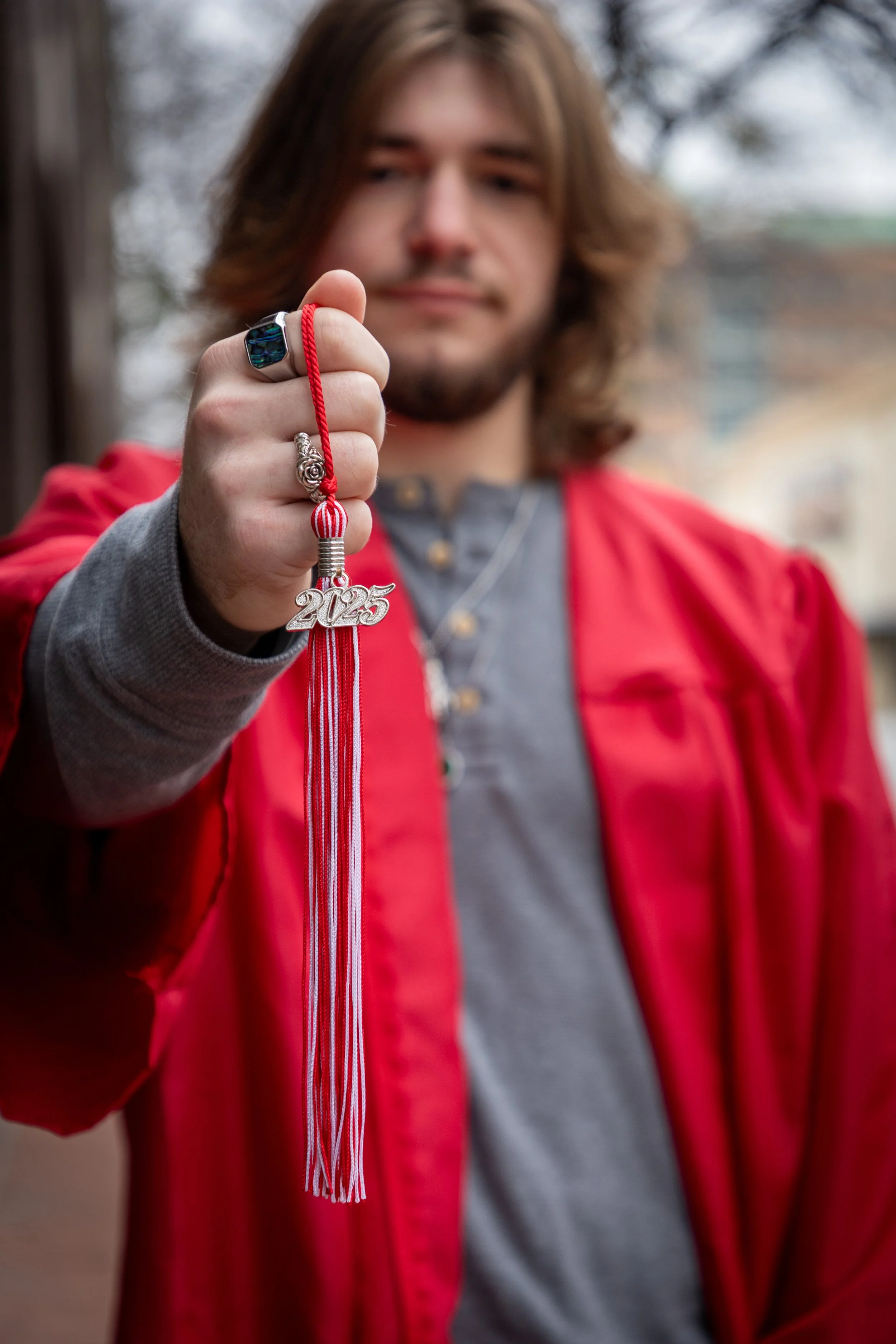 A young man in a red jacket holds up a graduation tassel with the year '2025' on it.