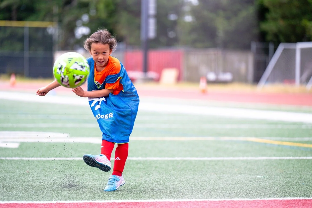 Young girl playing soccer on a field, kicking a green and white soccer ball.