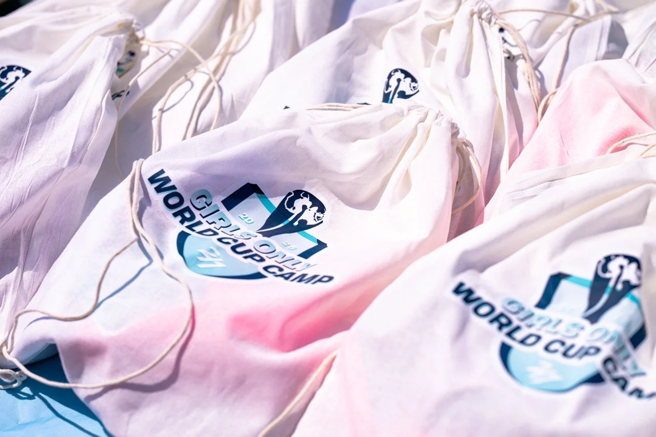 White drawstring bags with the 2023 FIFA Women's World Cup logo printed on them, piled together.