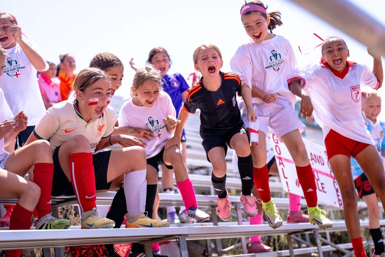 Children participating in a soccer event, jumping off bleachers with excited expressions, some wearing soccer jerseys and face paint.