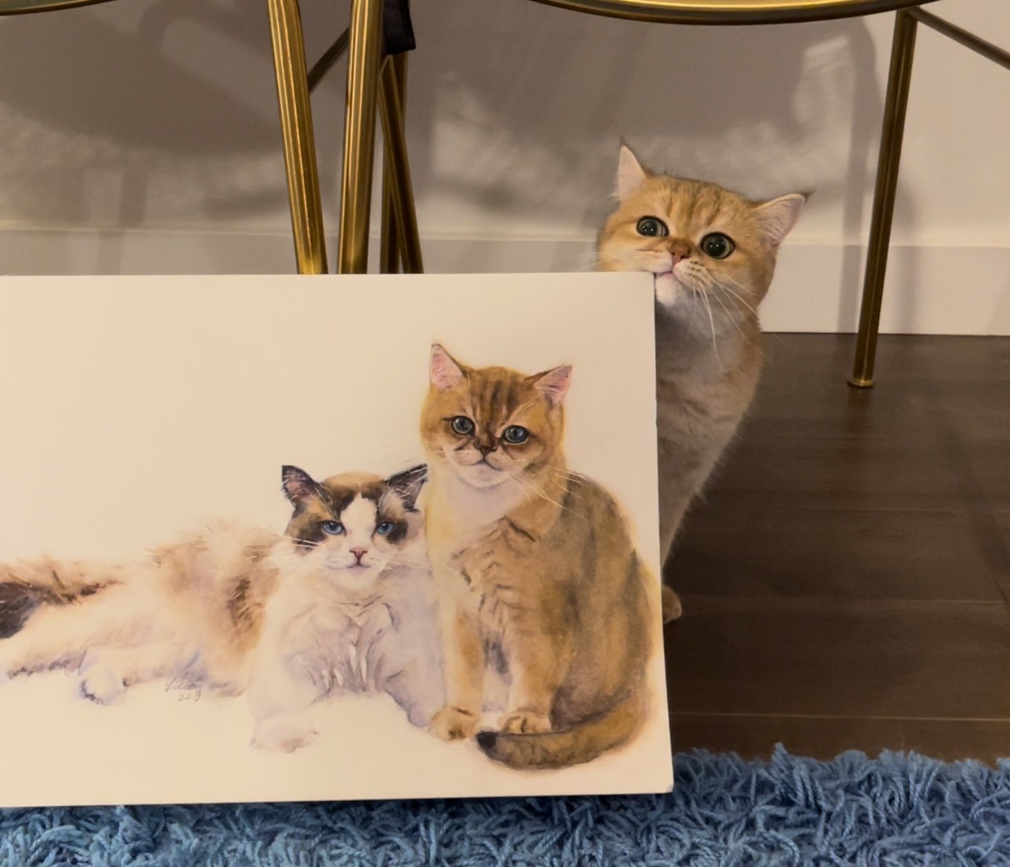 Cat posing behind a custom watercolor portrait of two cats