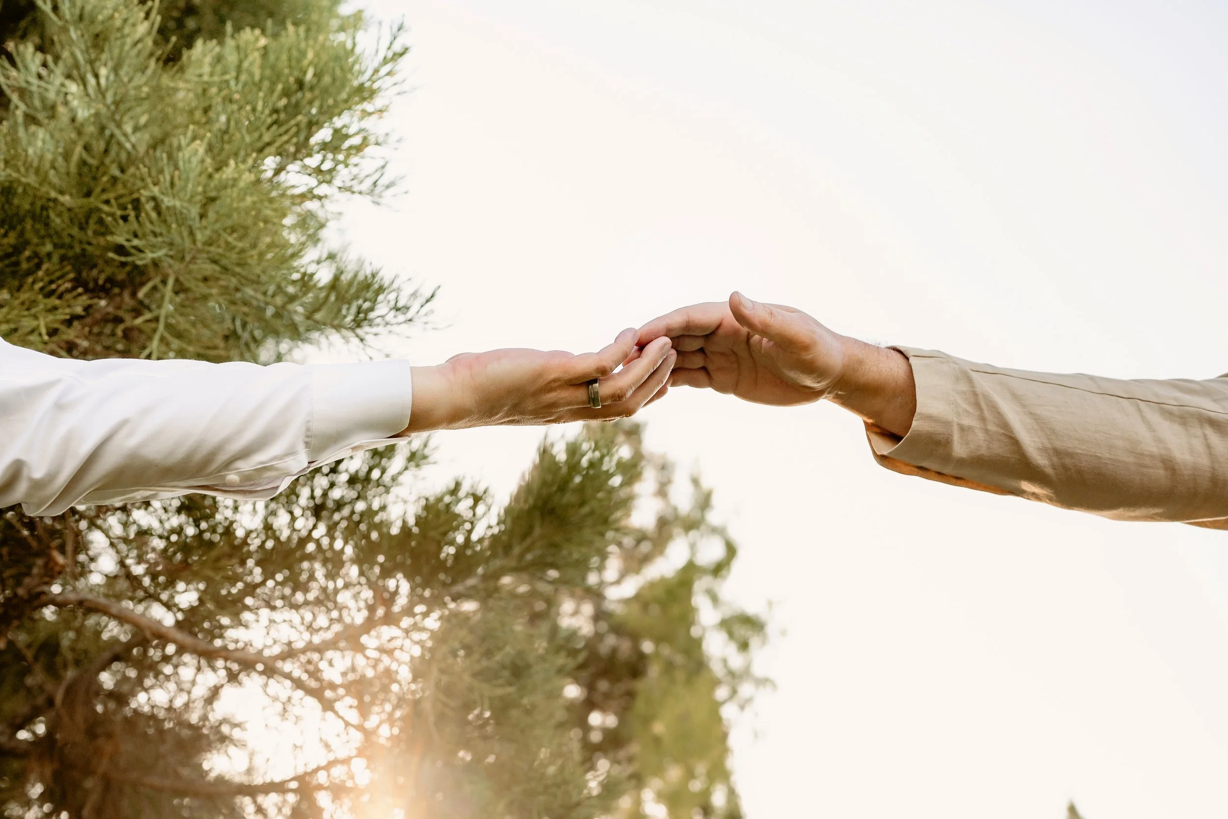Two people reaching out to touch their hands against a backdrop of trees and sky.